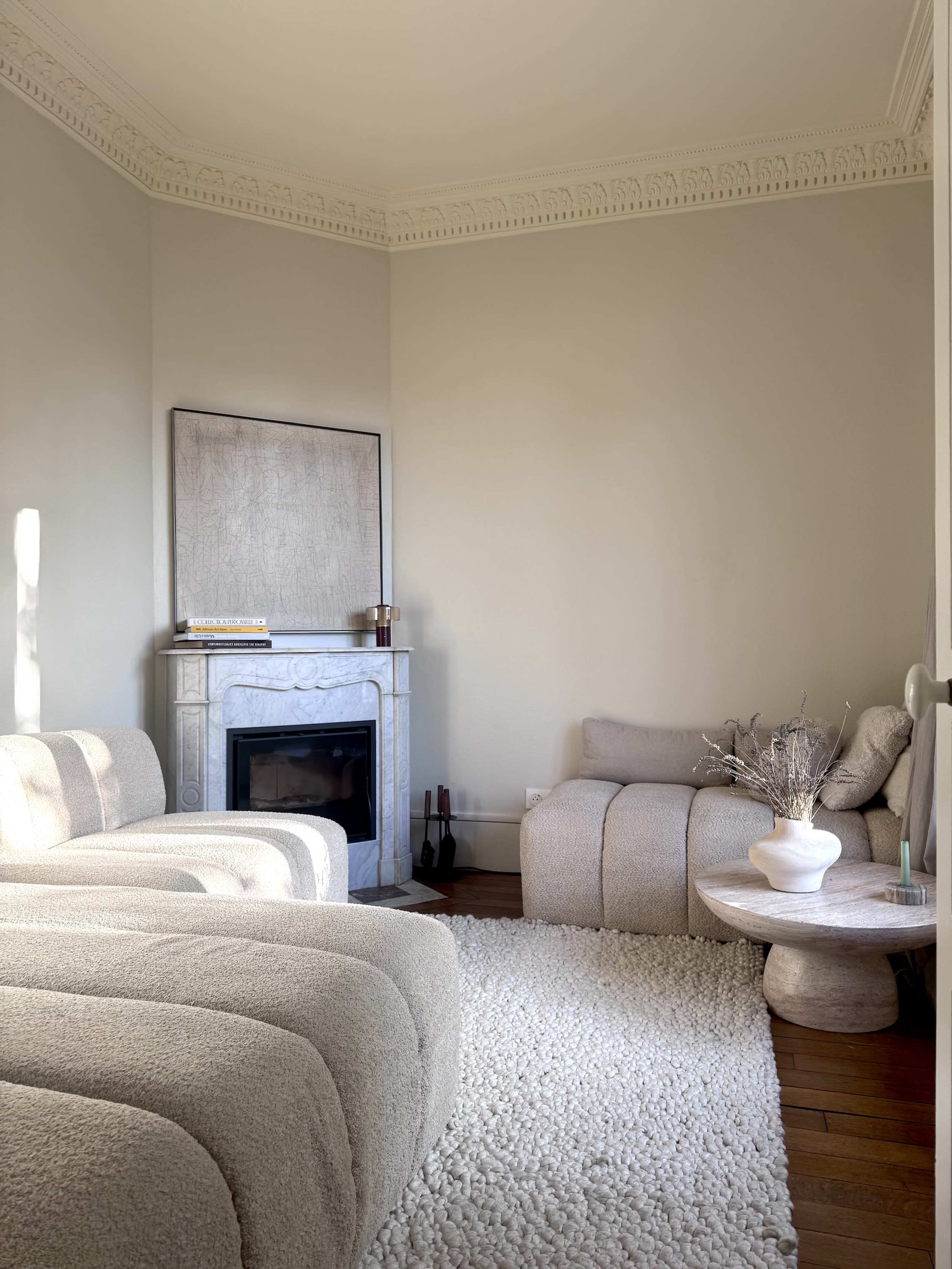 A cozy living room features two textured sofas, a circular side table, and a decorative fireplace against a light-colored wall.