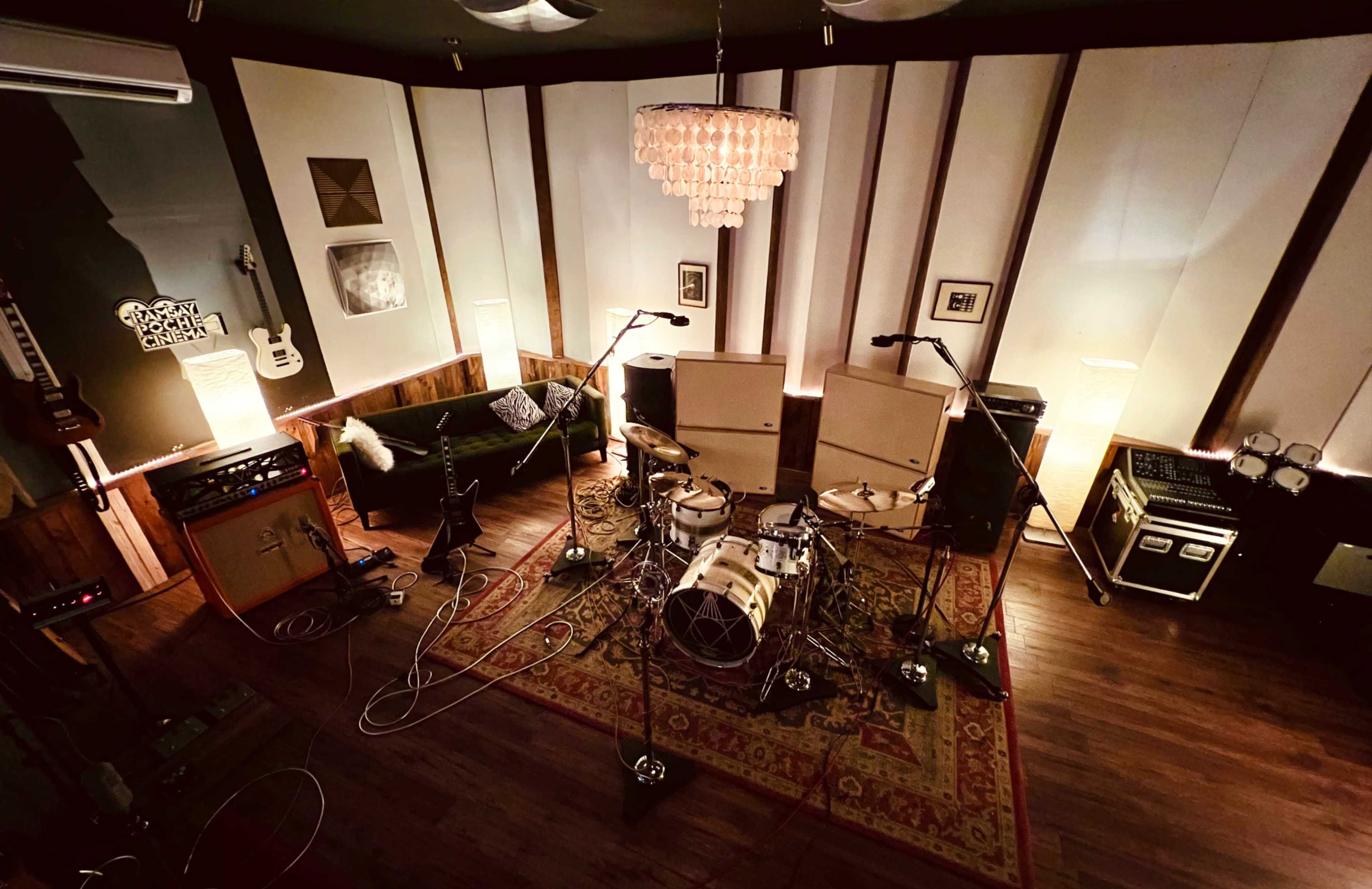A recording studio setup featuring a drum kit, amplifiers, microphones, and instruments arranged around a plush rug under soft lighting.