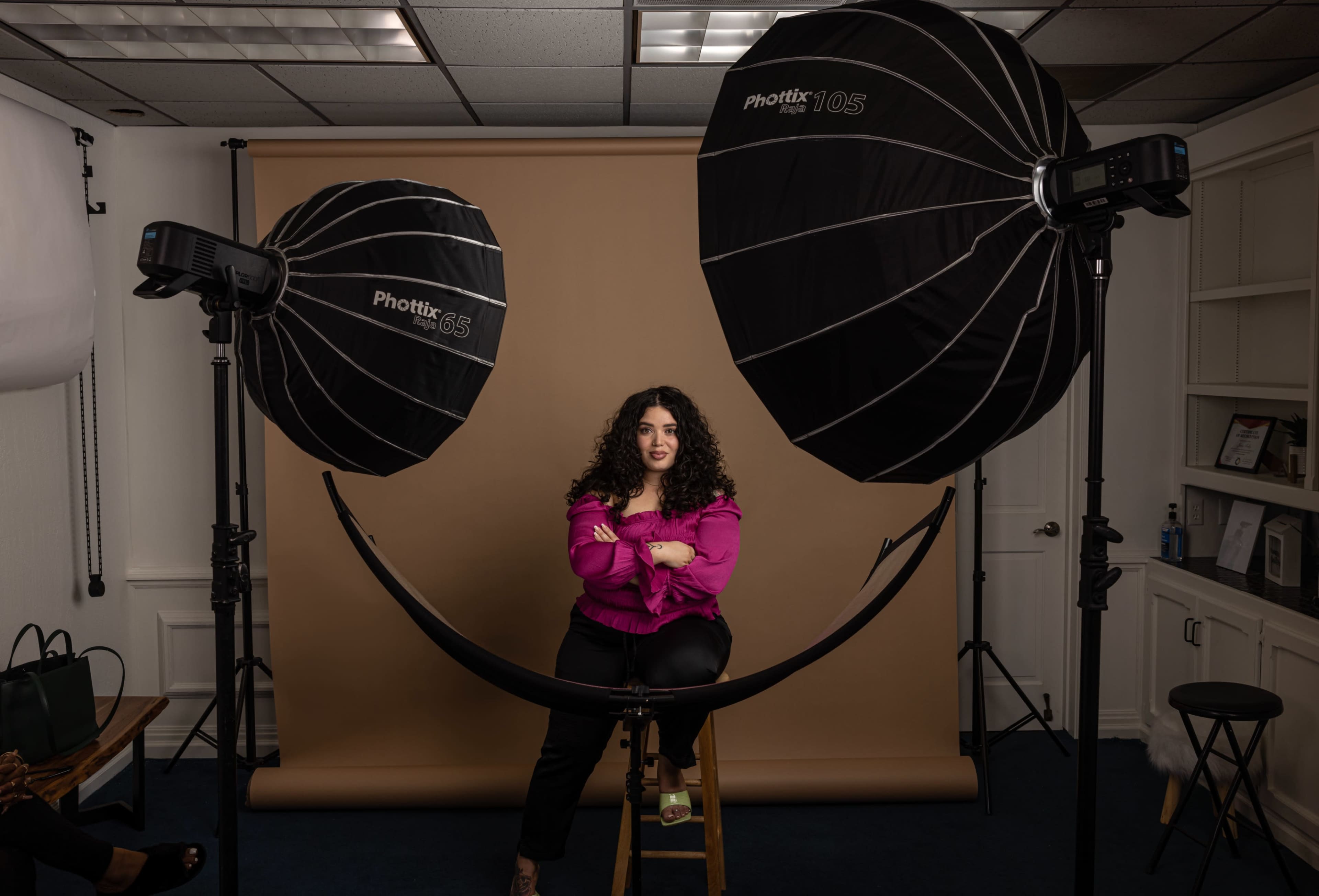 A person sits on a stool in front of a beige backdrop, illuminated by two large softbox lights on either side.