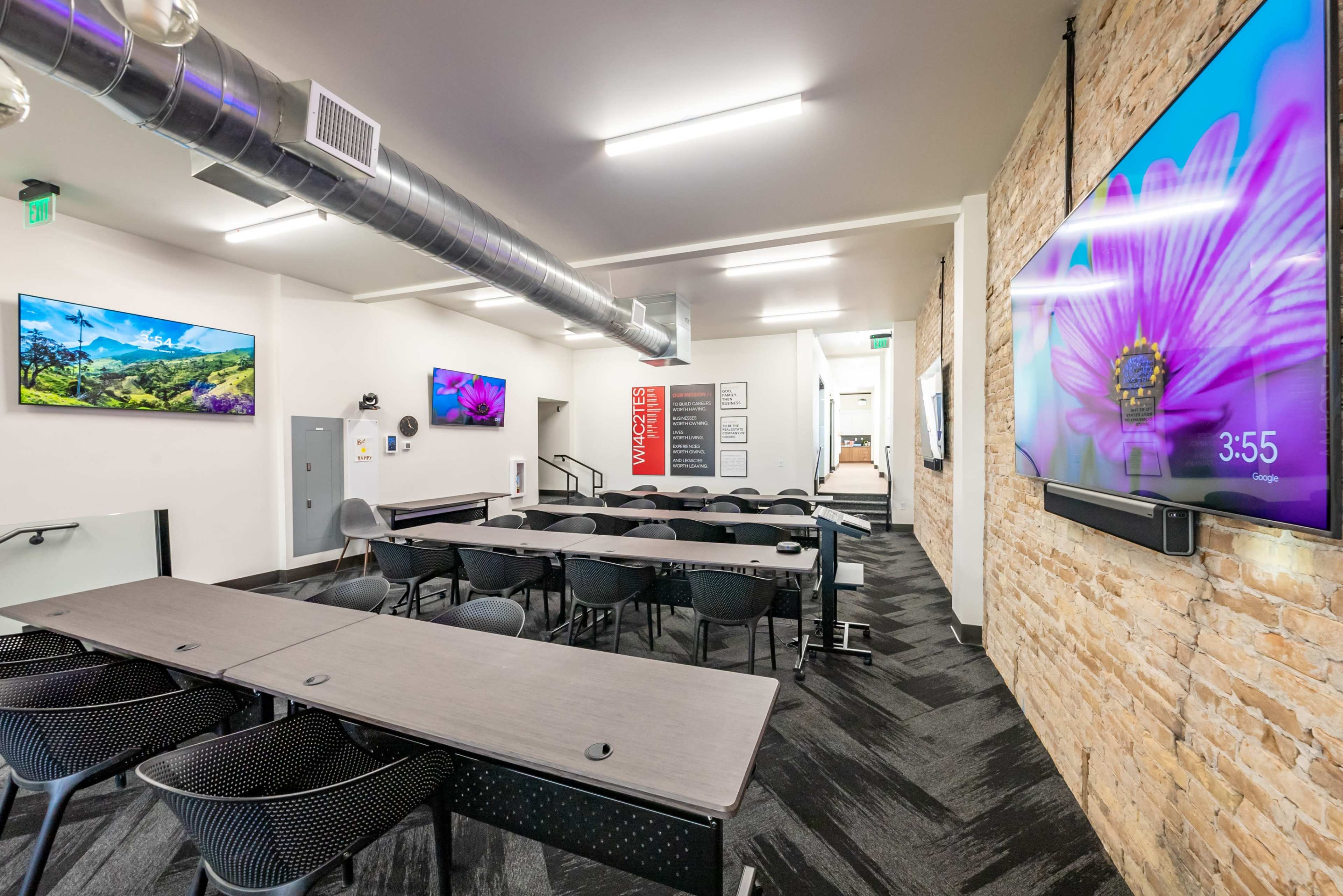 A modern conference room with long tables, black chairs, and two large screens mounted on the walls displaying vibrant images.