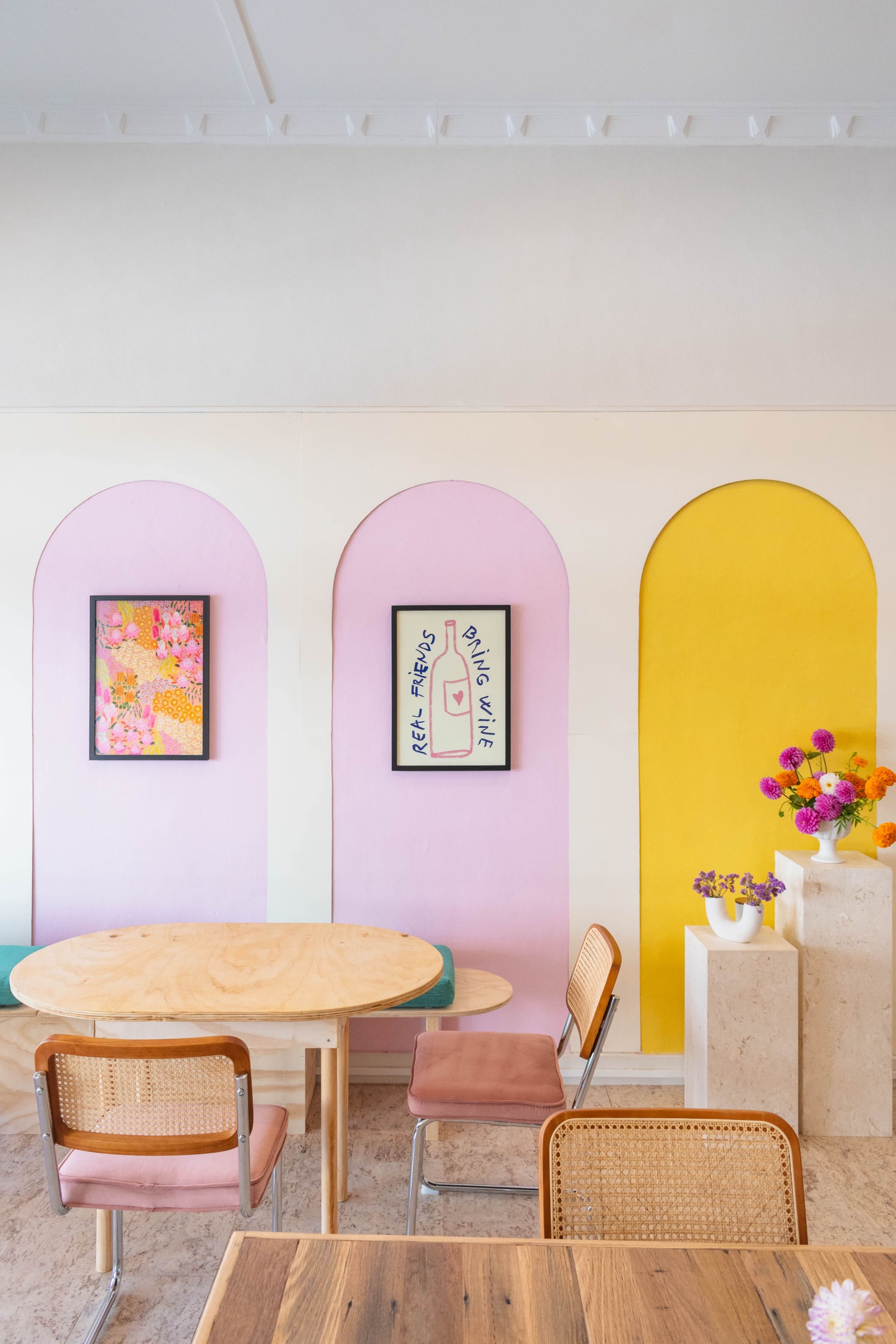 A cozy café interior featuring colorful archways with framed artwork, a round wooden table, and rattan chairs.