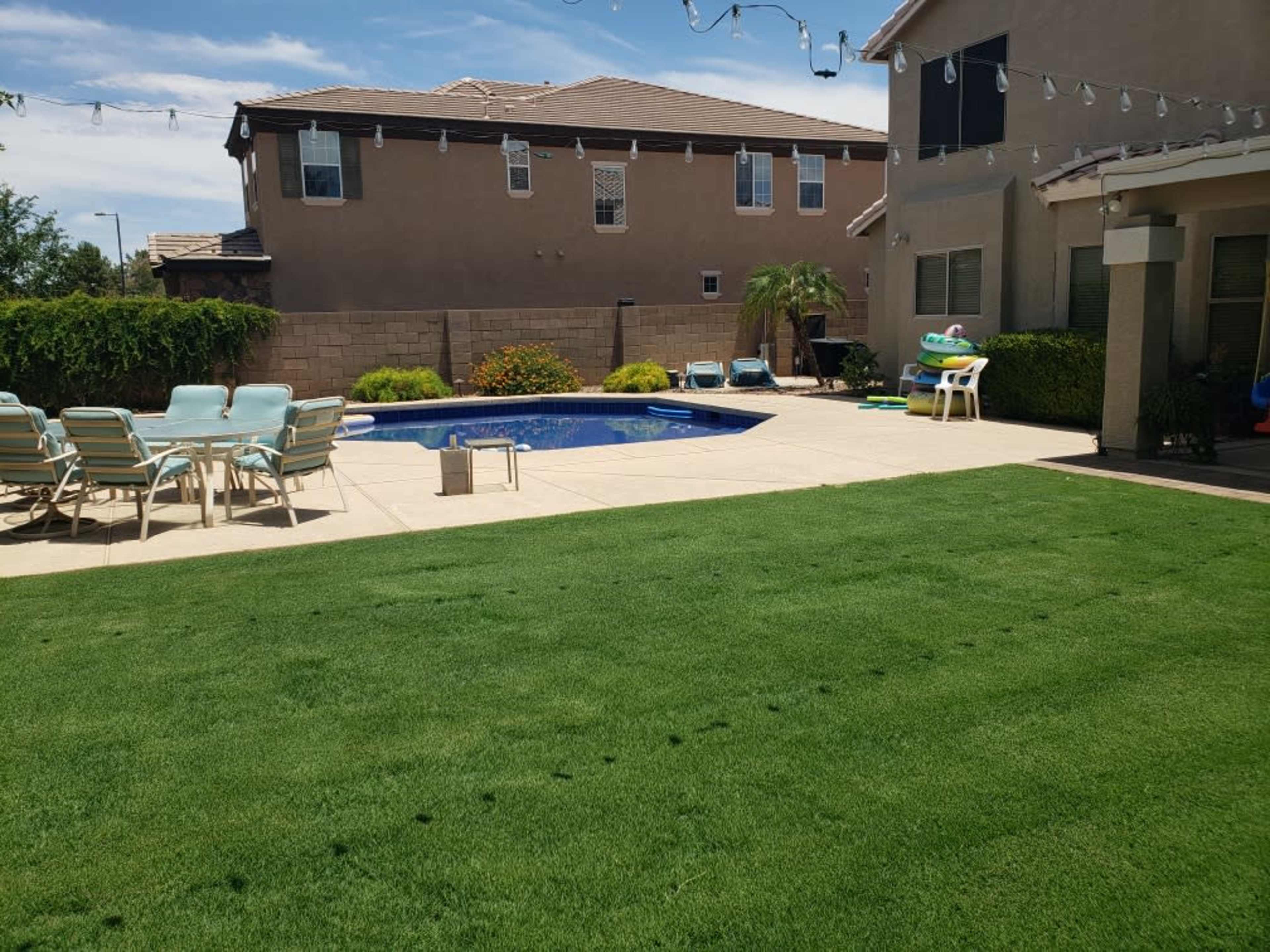 A well-maintained backyard features a swimming pool surrounded by lounge chairs and a neatly trimmed lawn.