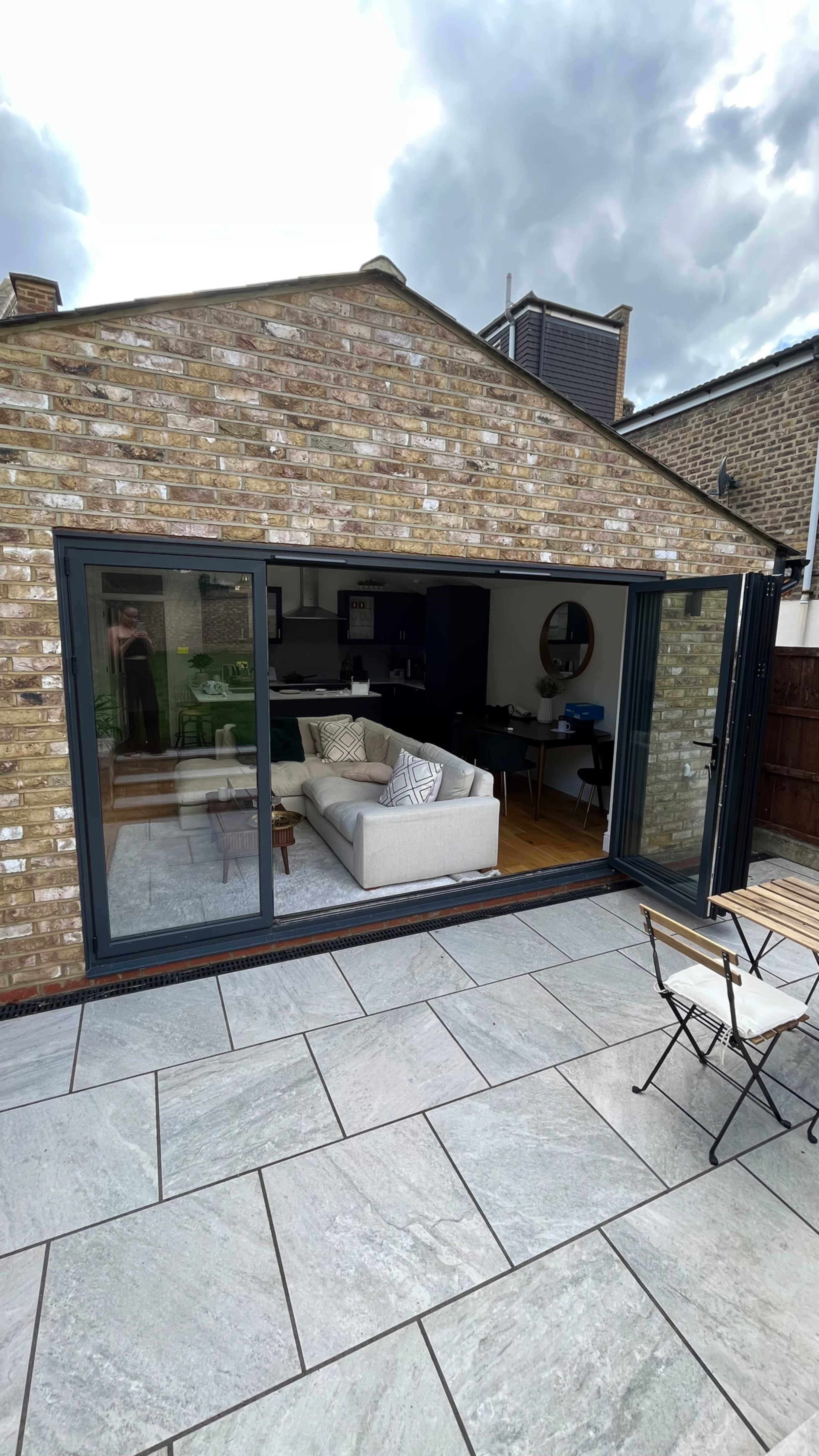 A modern living space with large glass doors opens onto a patio, featuring a light-colored sofa and wooden flooring inside.