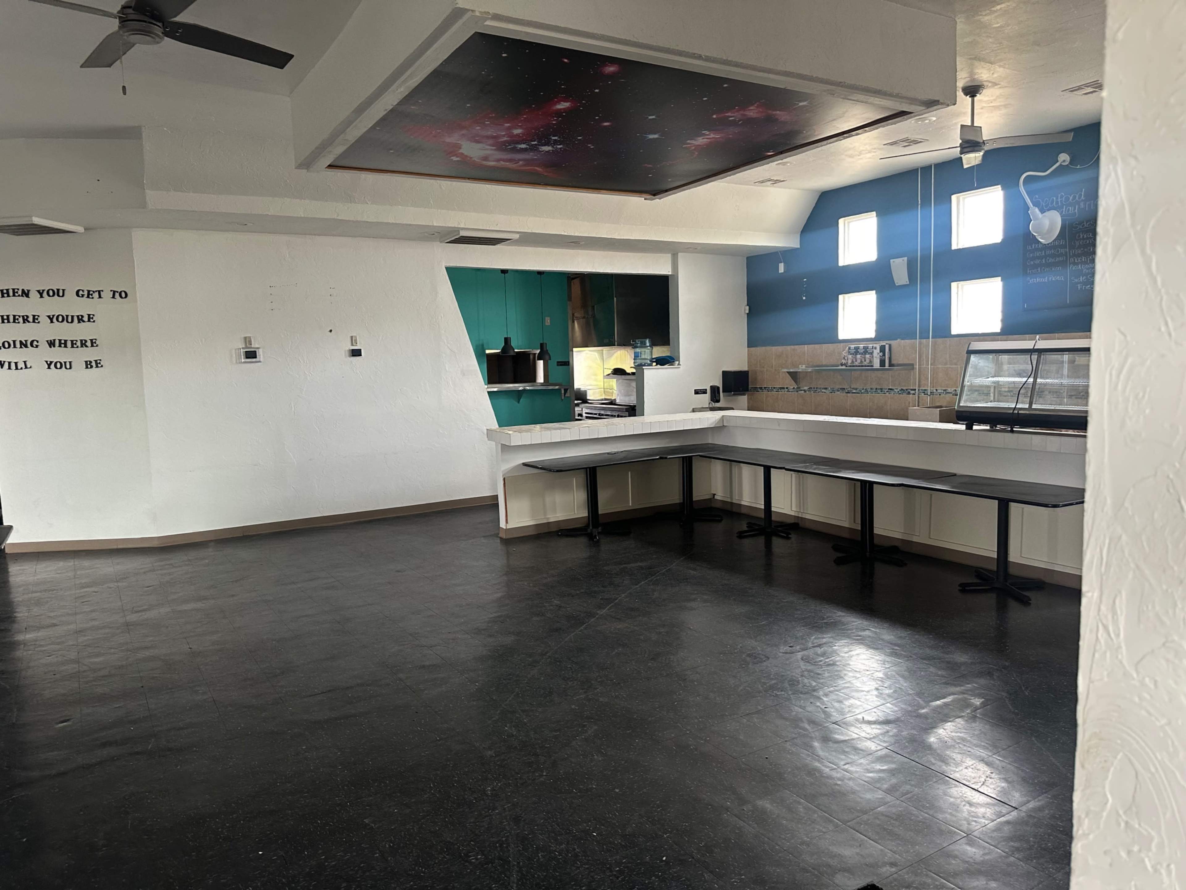 The image shows an empty room with a large counter, a few windows, and a decorative ceiling featuring a space-themed design.