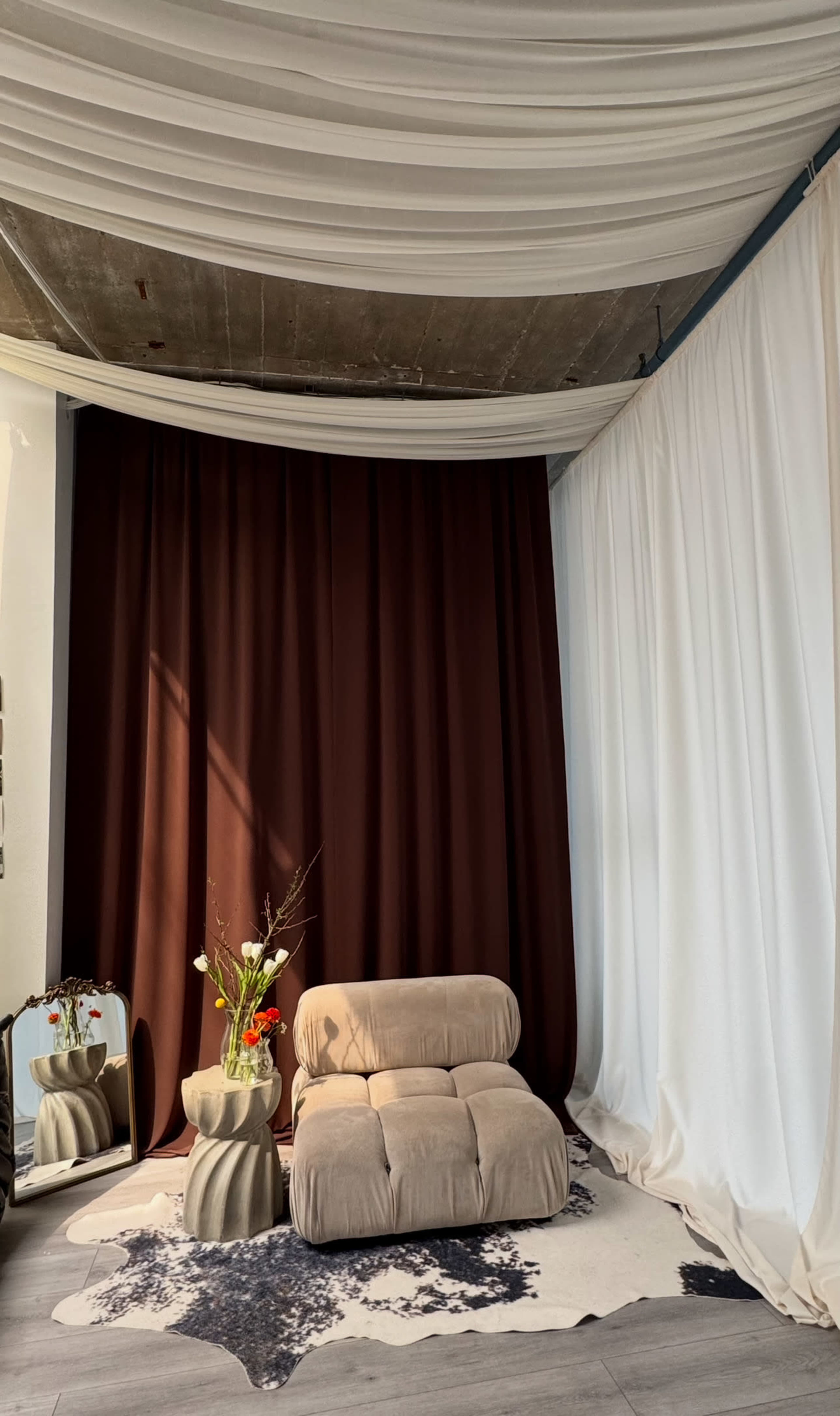 The scene features a cozy sitting area with a beige sofa, a round decorative table with flowers, a cowhide rug, and contrasting dark and light curtains.