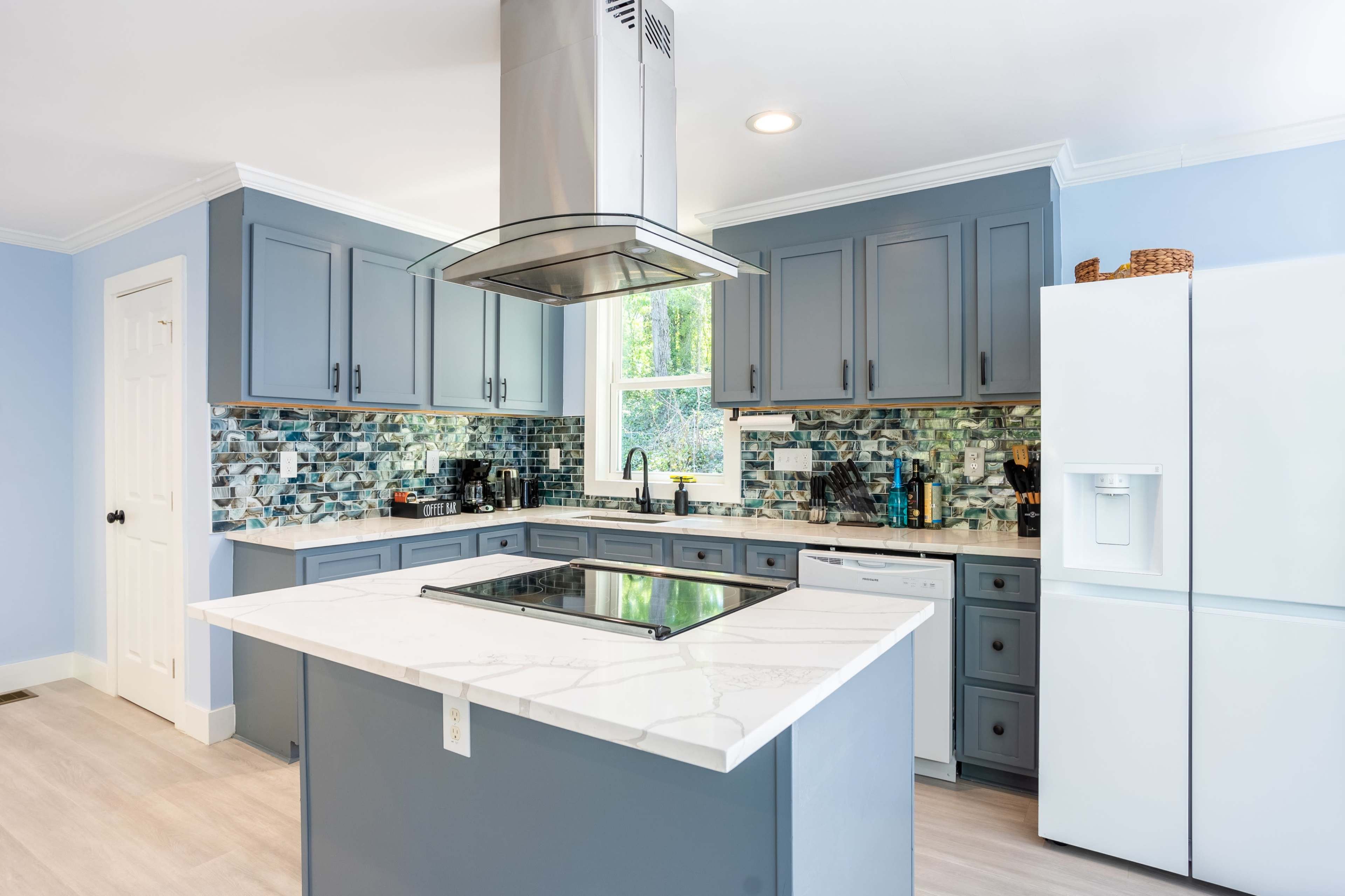 A modern kitchen features grey cabinetry, a large island with a marble countertop, and a stainless steel range hood.