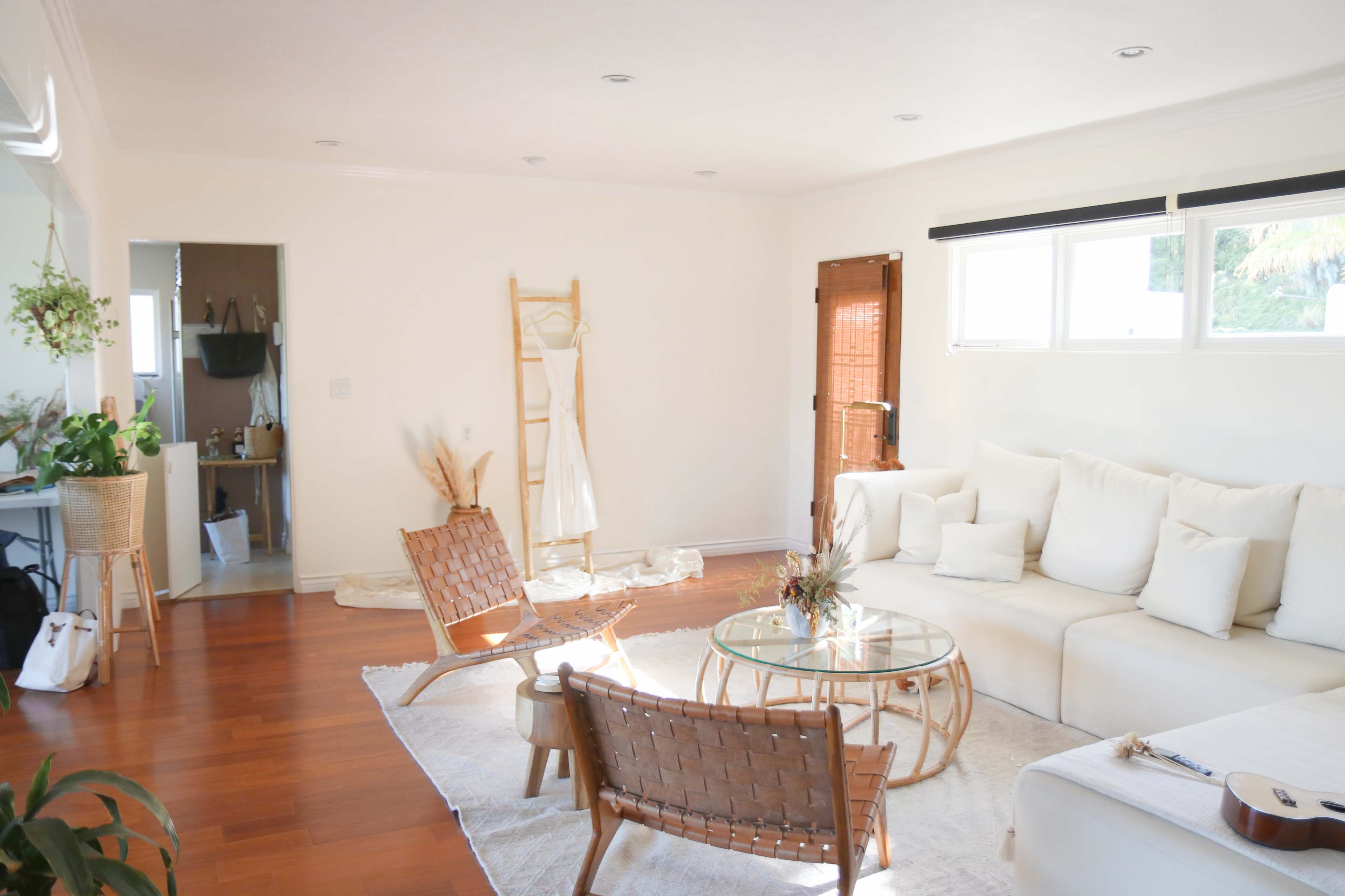 A bright, simple living room with a large white sectional sofa, wicker chairs, a round glass coffee table, and a light-colored area rug.