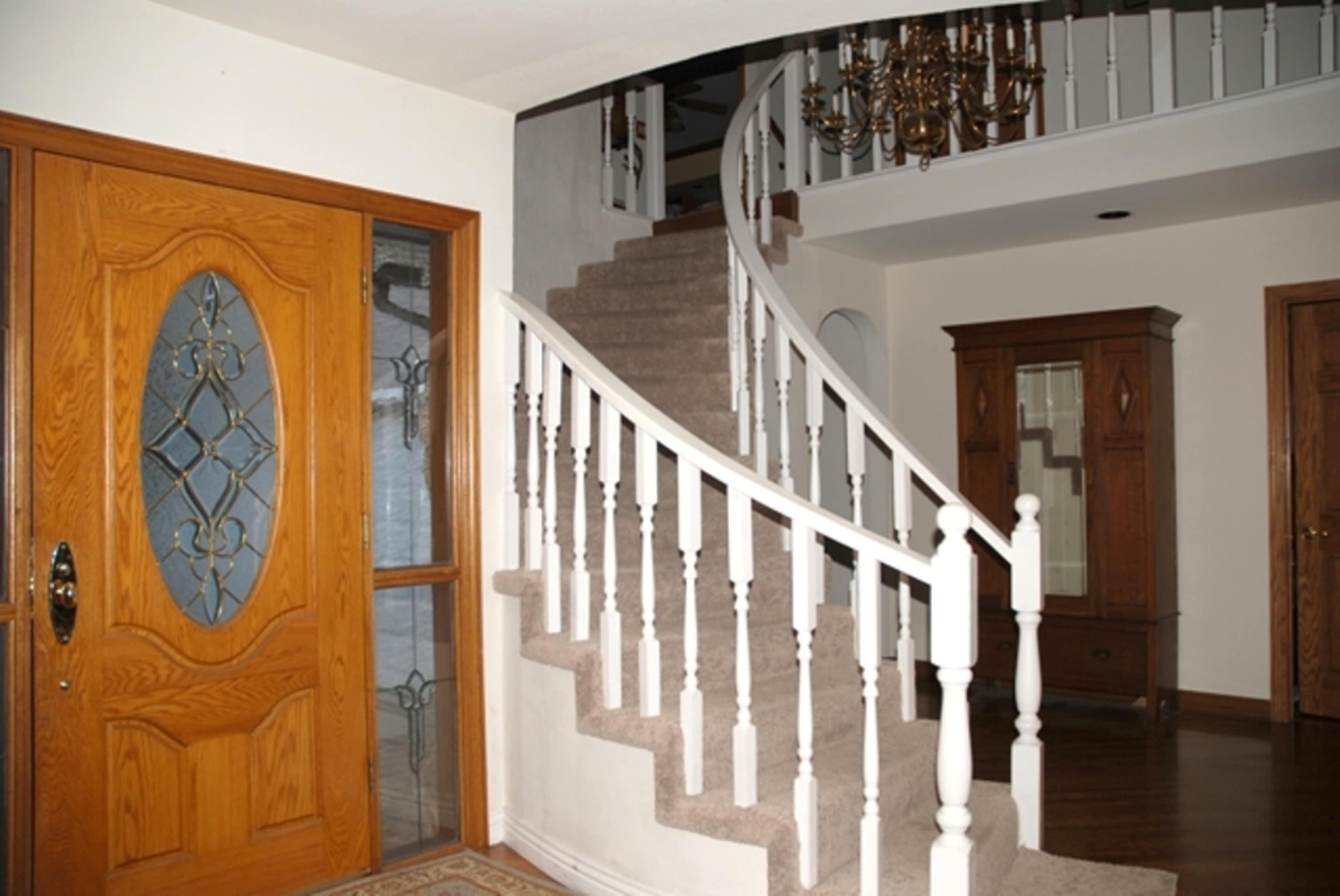 An entrance hallway with a wooden door, a carpeted spiral staircase, and a chandelier overhead.