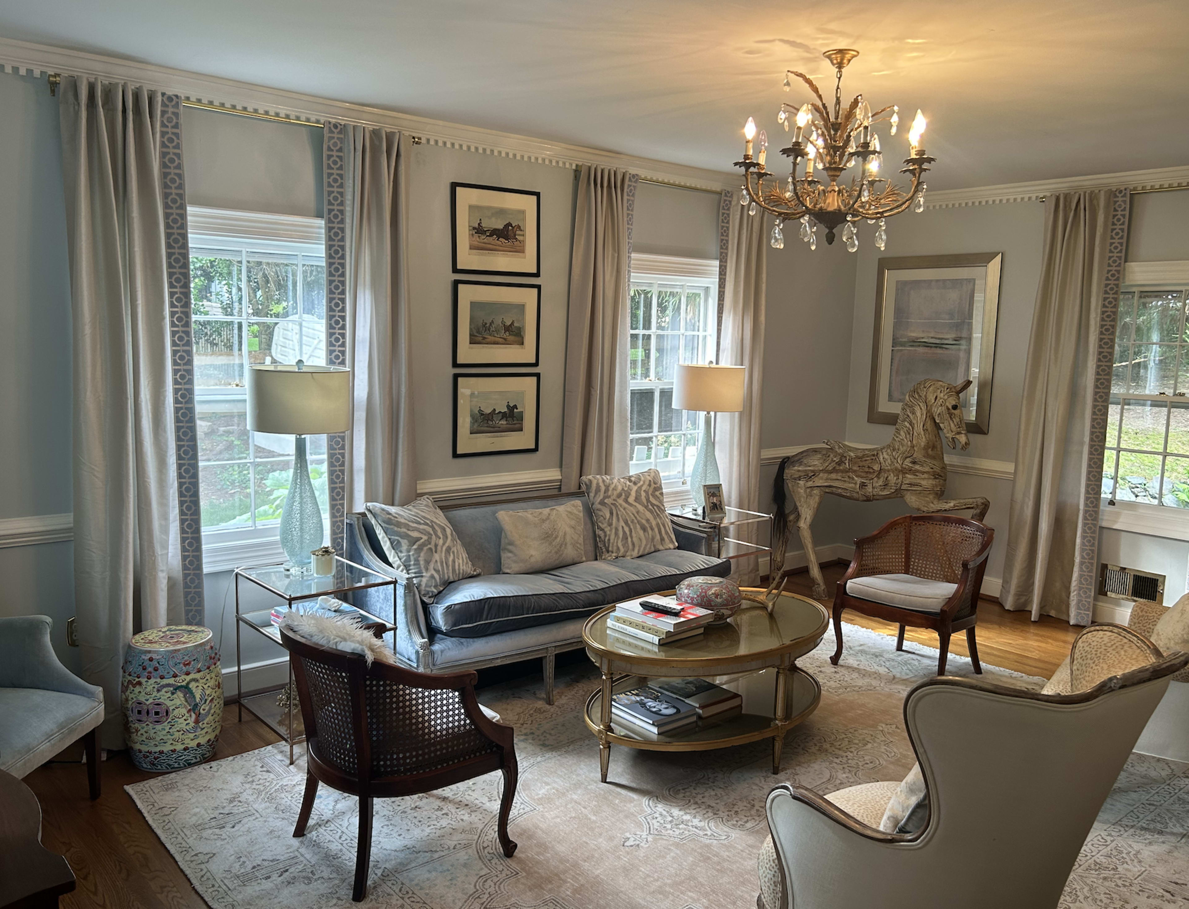 A well-furnished living room featuring a blue sofa, a round coffee table, two armchairs, and large windows with sheer curtains.