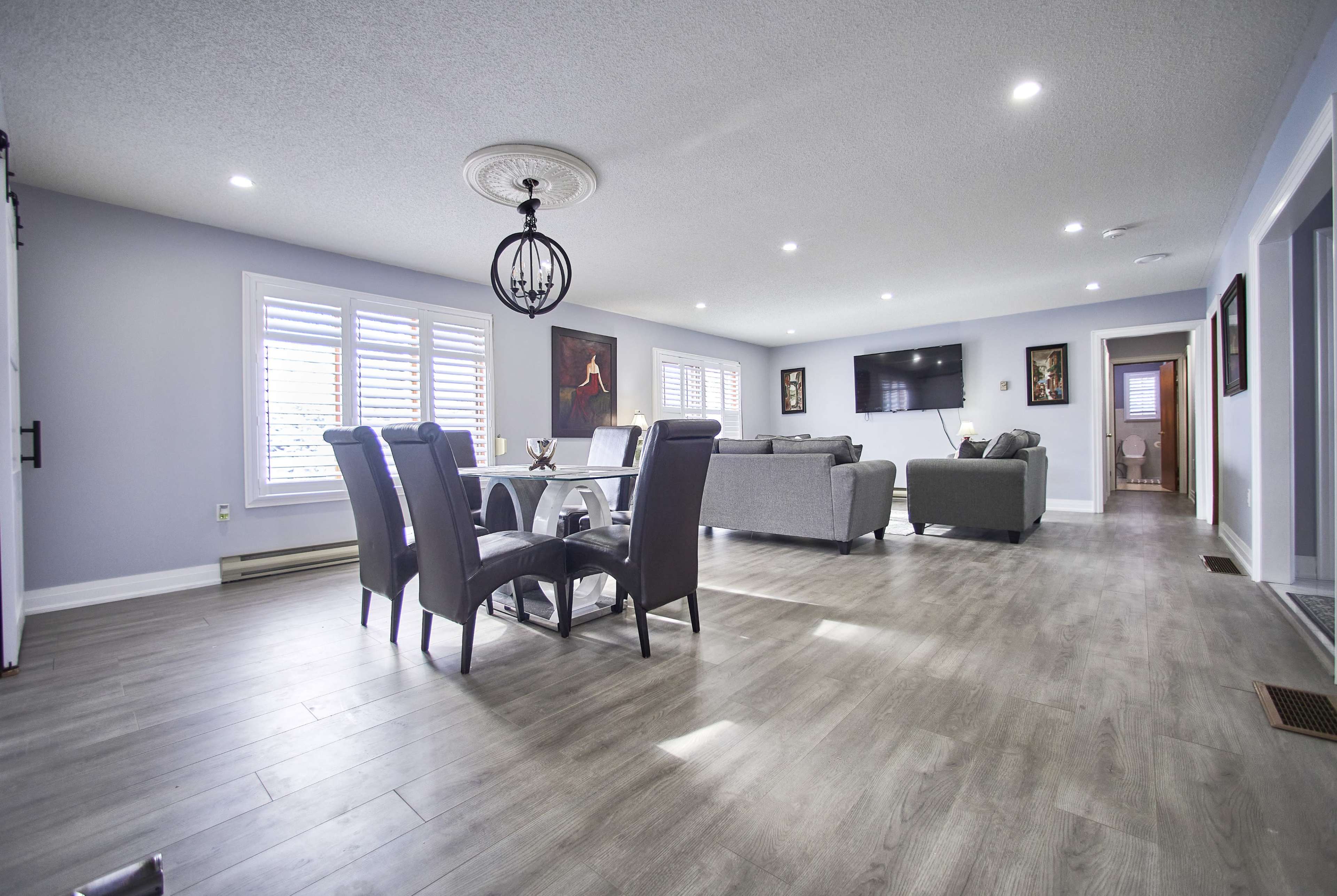 A well-lit living space with a dining area featuring a table and six chairs, a couch set, and a wall-mounted television.
