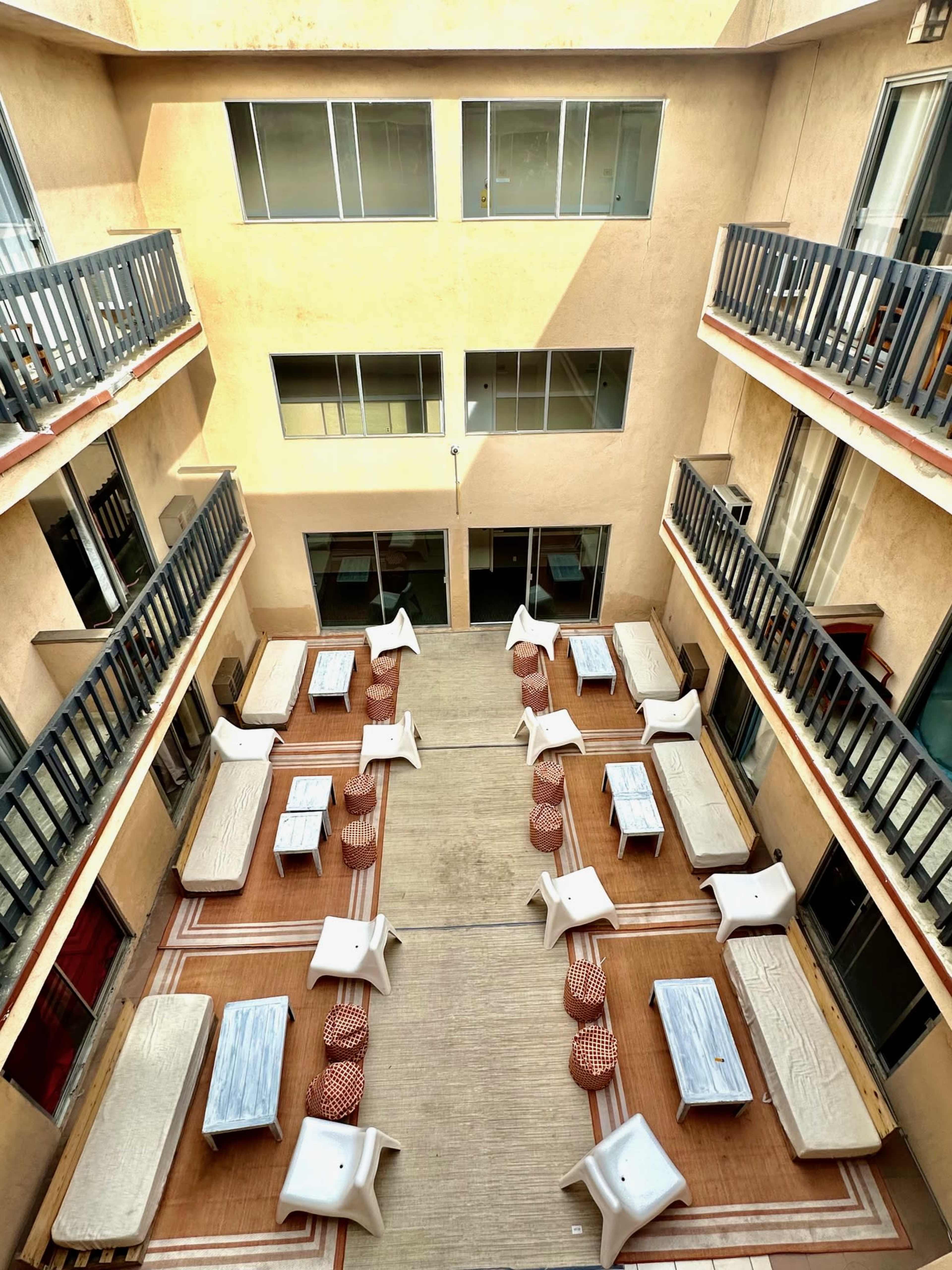The image shows an open-air courtyard filled with tables and chairs arranged in rows, surrounded by walls with balconies.
