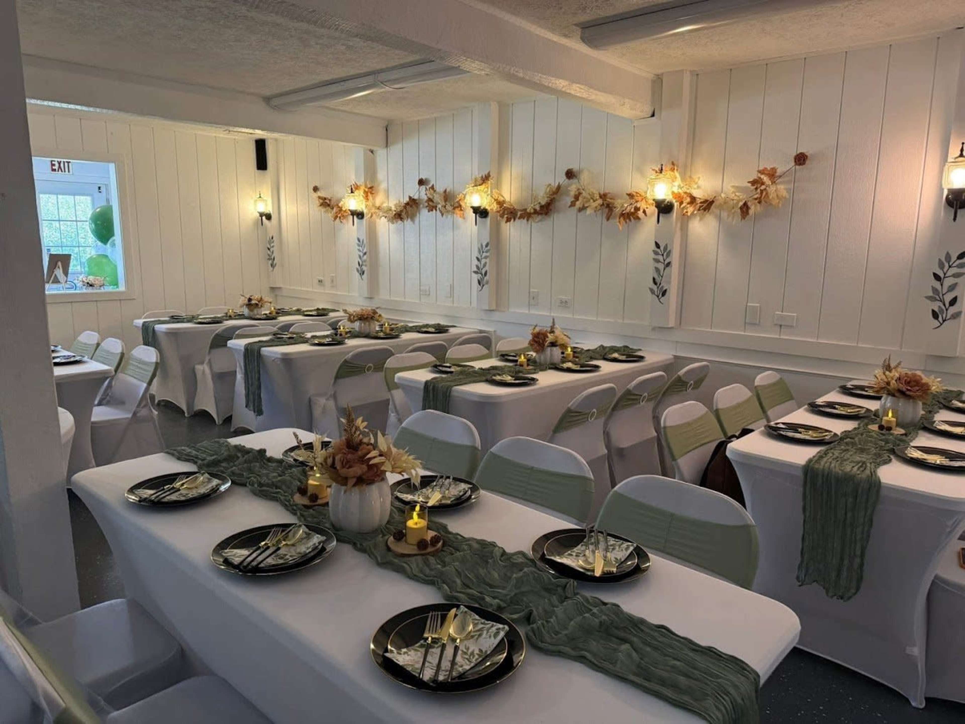 The image shows a neatly arranged dining room with tables covered in white tablecloths, adorned with green runners and elegant place settings.