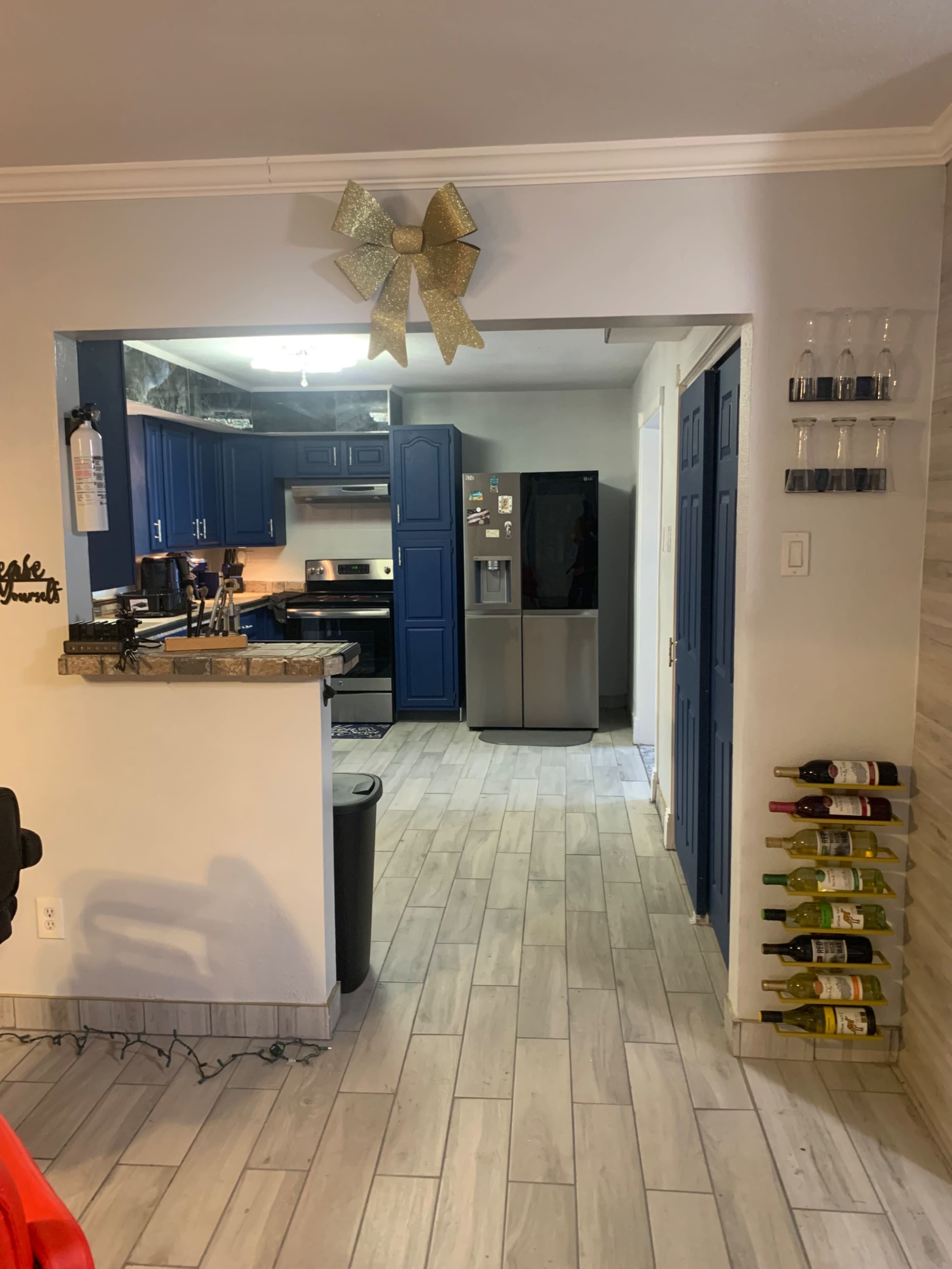 The image shows a kitchen with blue cabinets, a stainless-steel refrigerator, and a wall-mounted rack holding several bottles of wine.