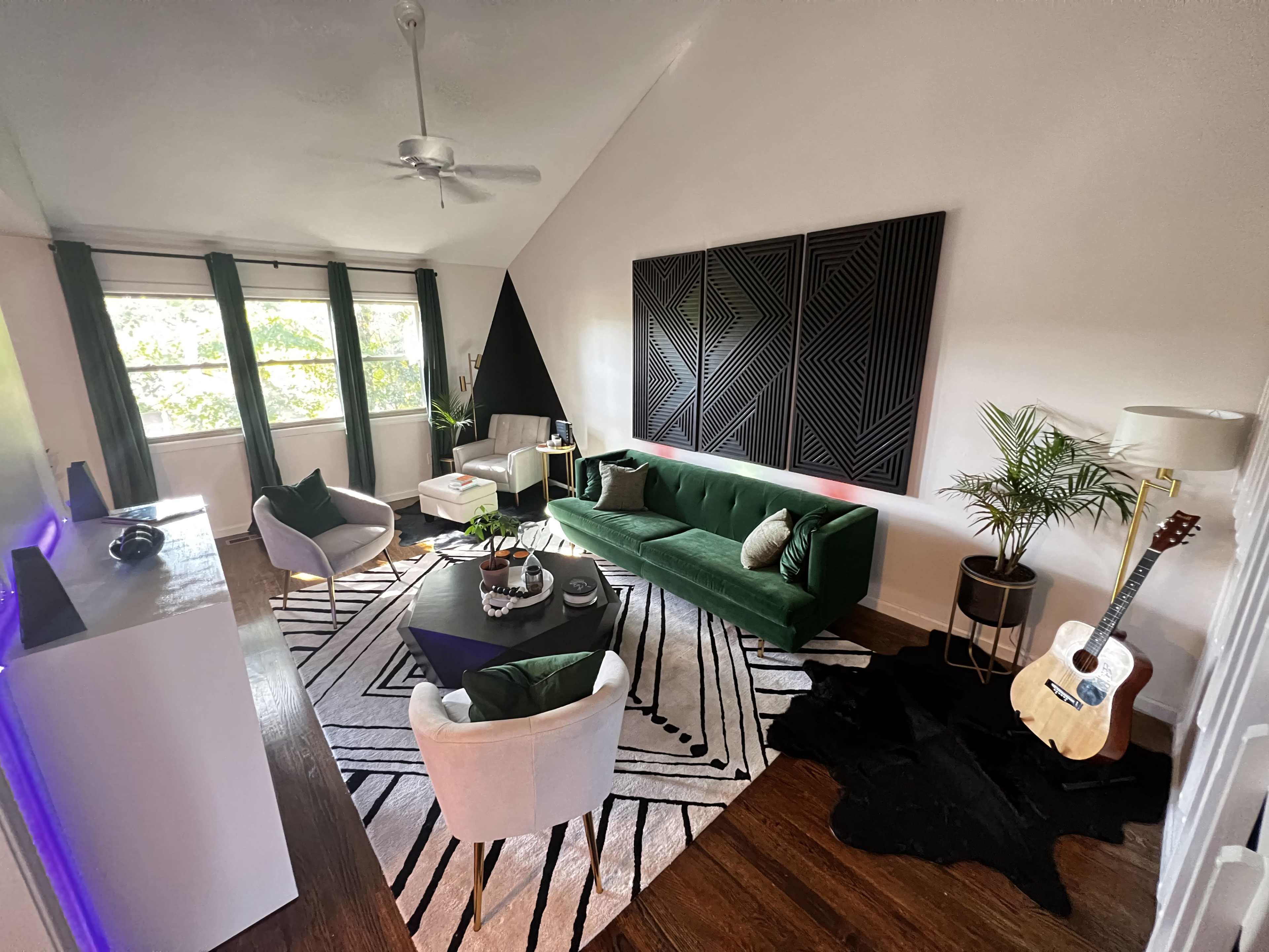 A modern living room featuring a green sofa, a round coffee table, a patterned rug, and large windows allowing natural light to fill the space.