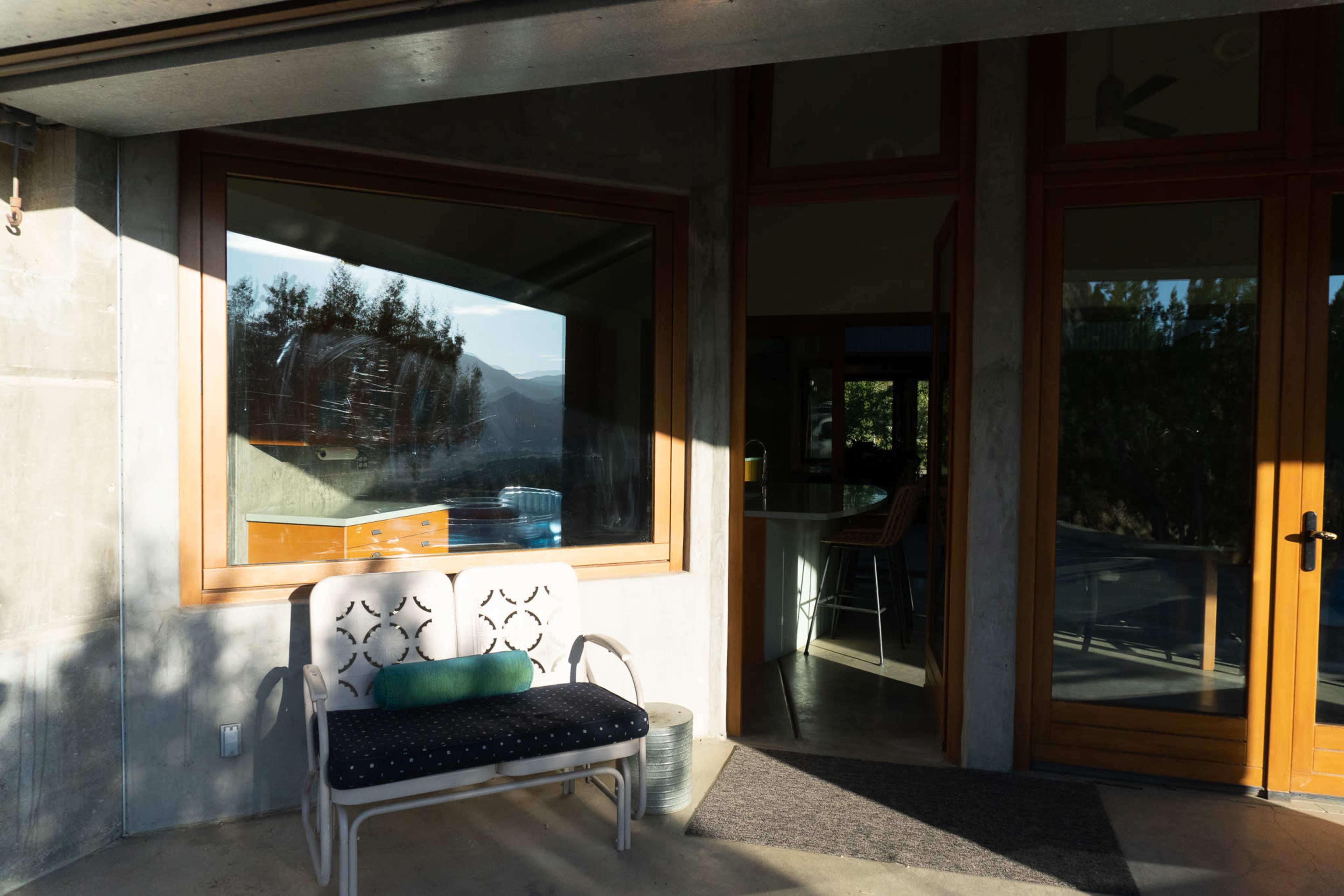 A bench sits in front of a modern glass window and wooden door, featuring a view of trees and mountains.