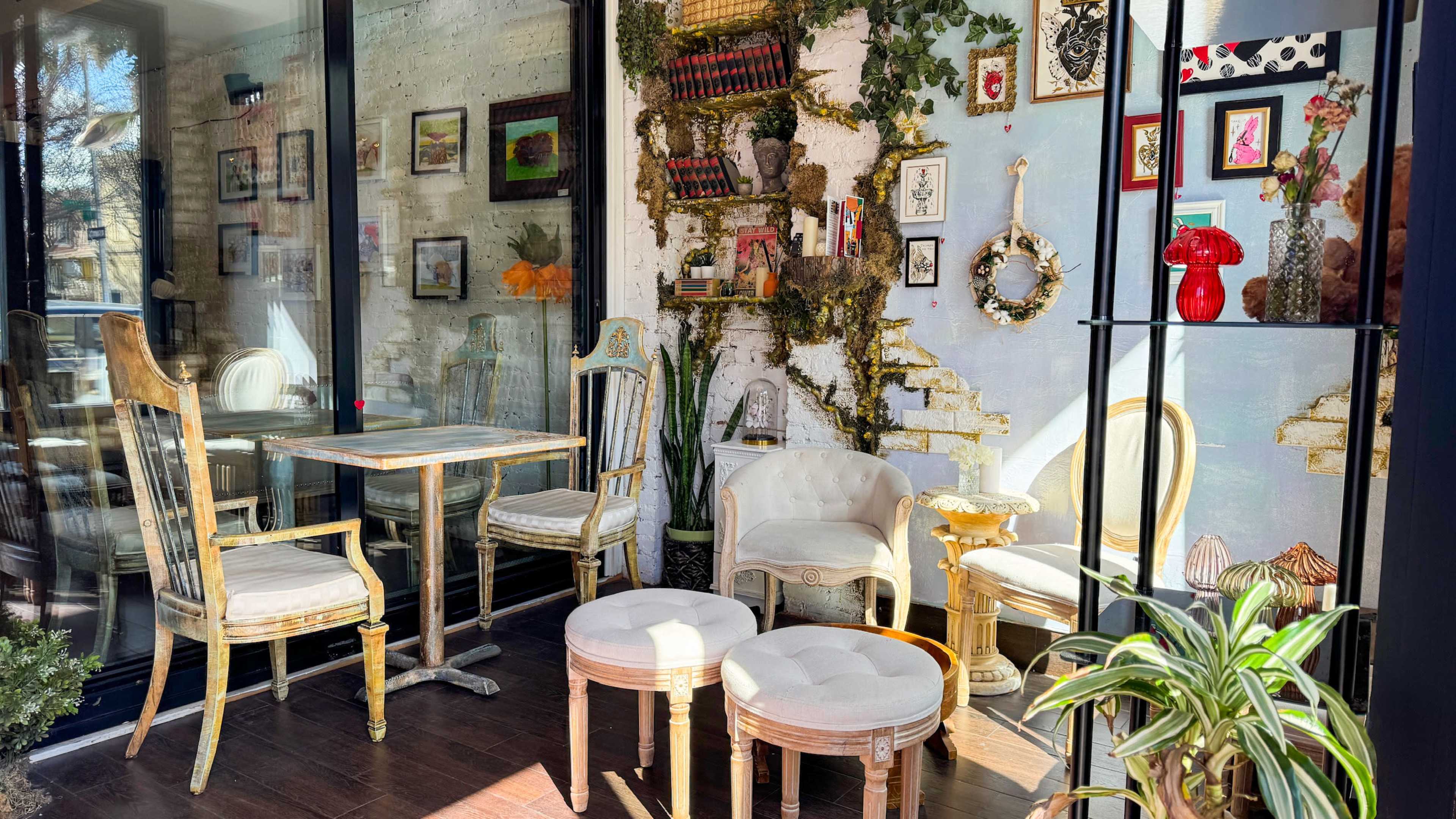 A cozy café interior with vintage seating, framed artwork on the walls, and decorative plants.