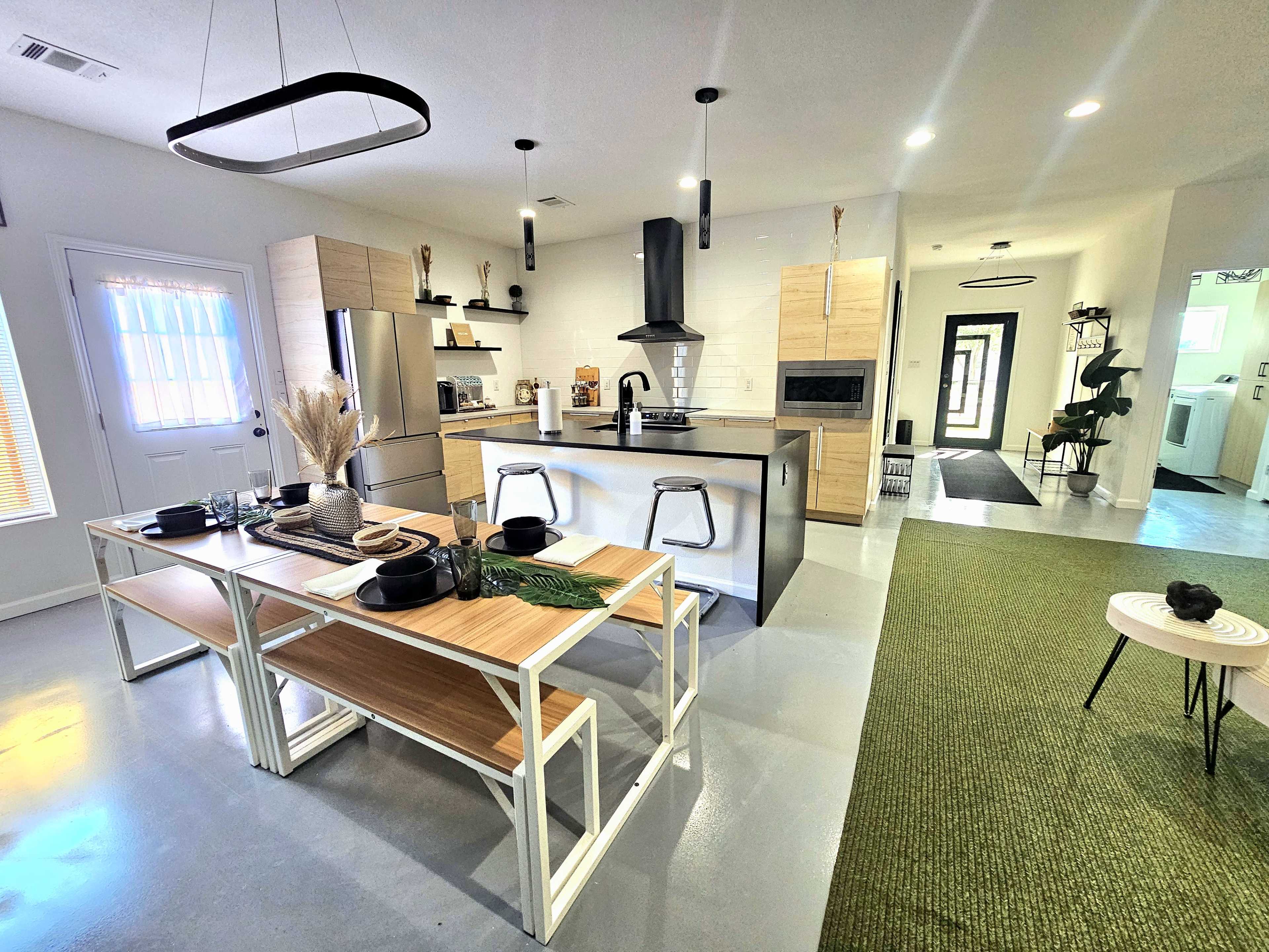 A modern kitchen and dining area featuring a large wooden table, sleek bar stools, and cabinetry in neutral tones.