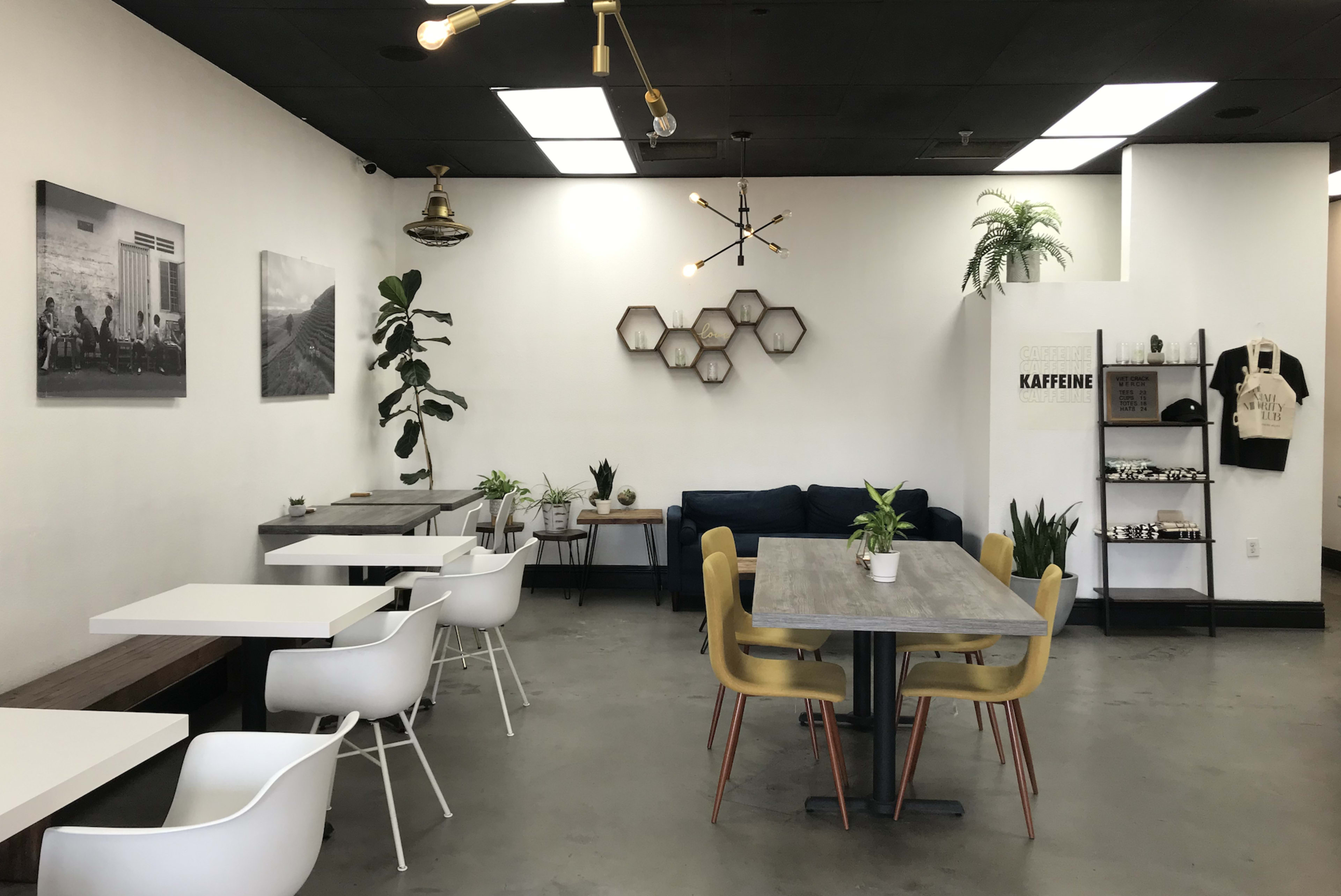 A modern café interior with minimalist furniture, including white chairs and wooden tables, alongside plants and wall art.