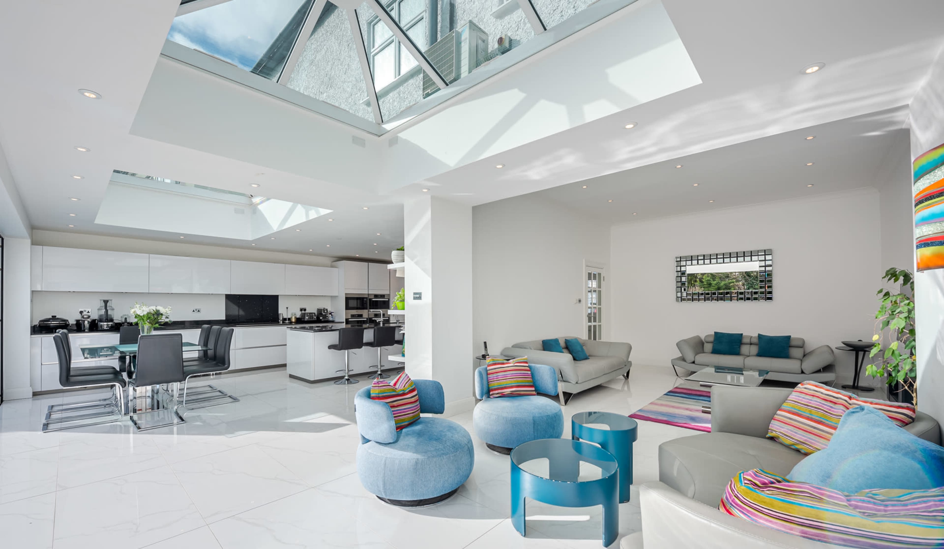 A modern open-plan living area with a skylight, featuring a kitchen, dining table, and colorful seating arrangements.