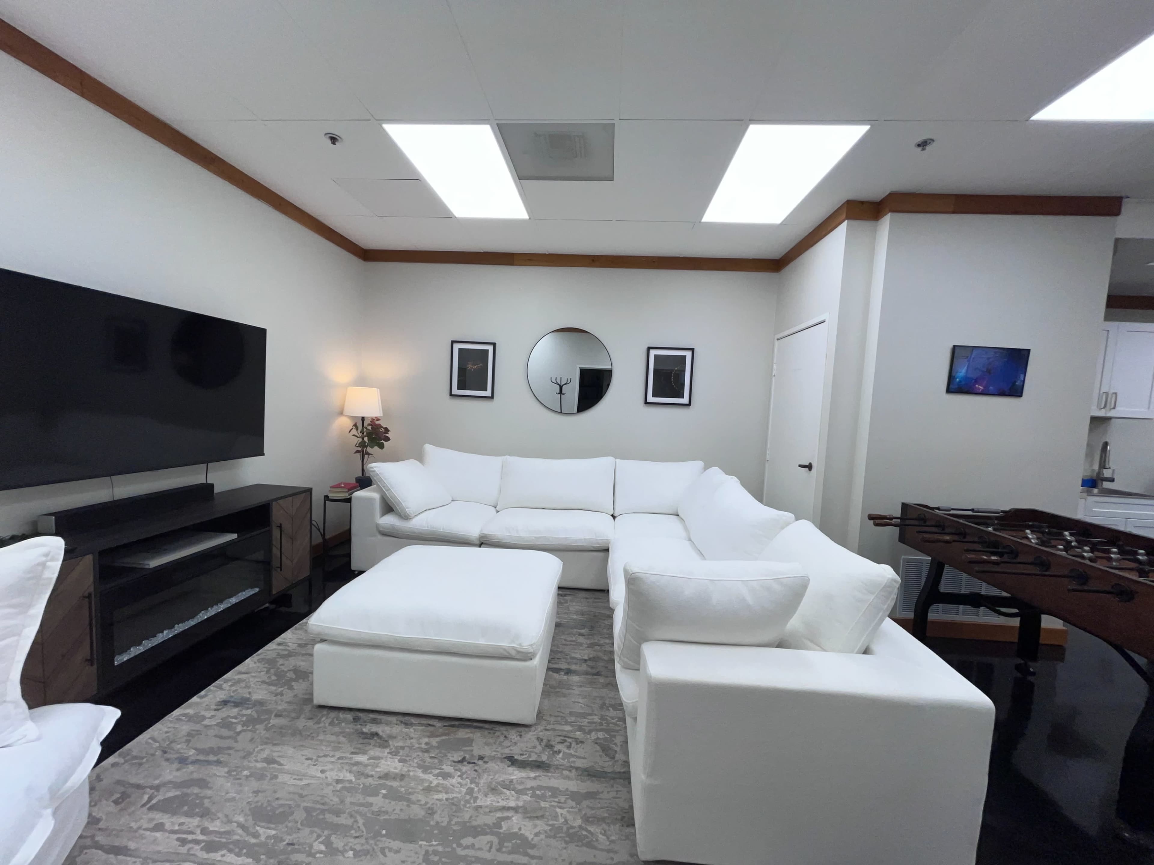 The living room features a large white sectional sofa, a coffee table, and a wall-mounted television against a neutral background.