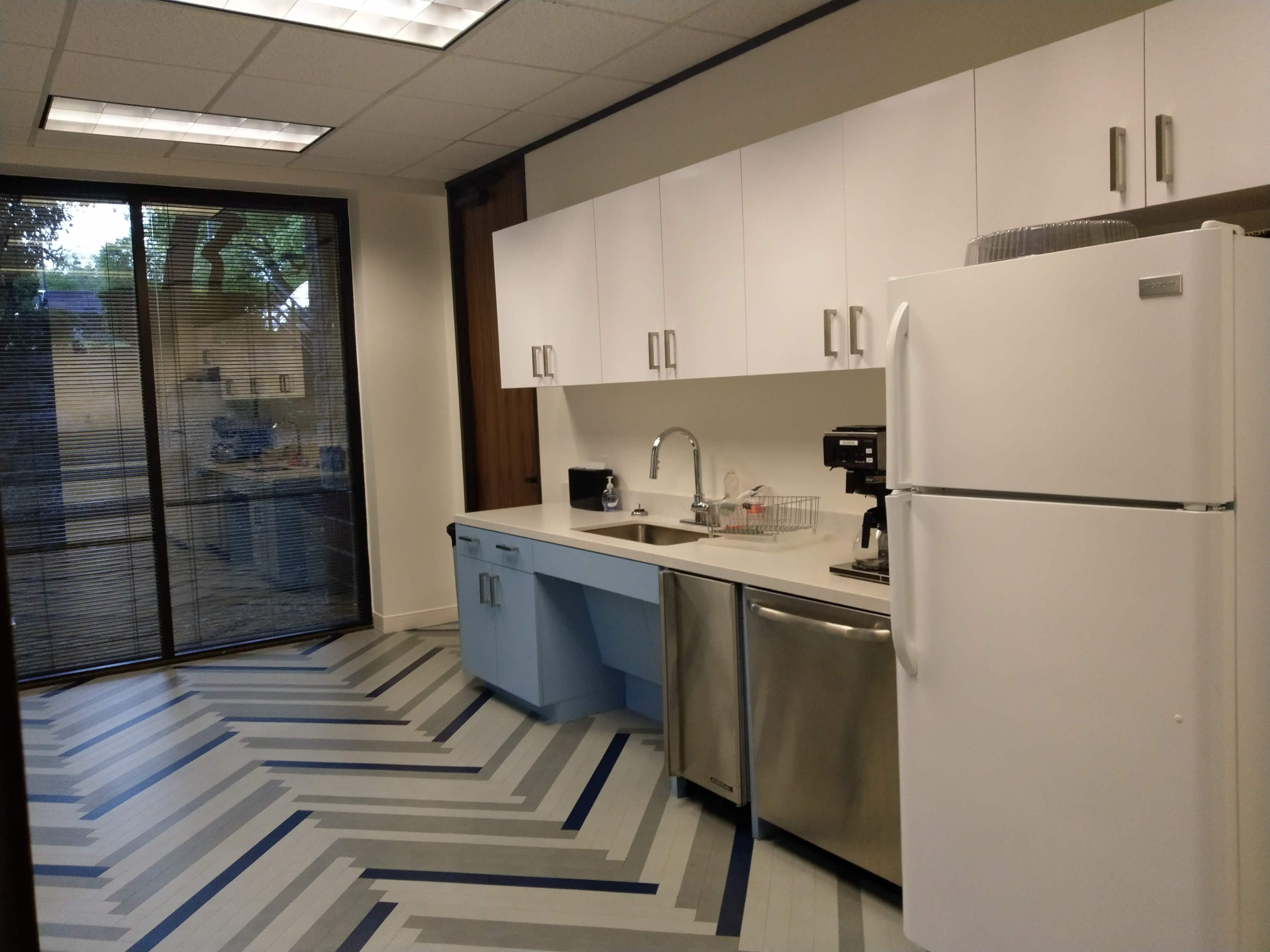 A modern kitchen area with white cabinets, stainless steel appliances, and a striped floor design.