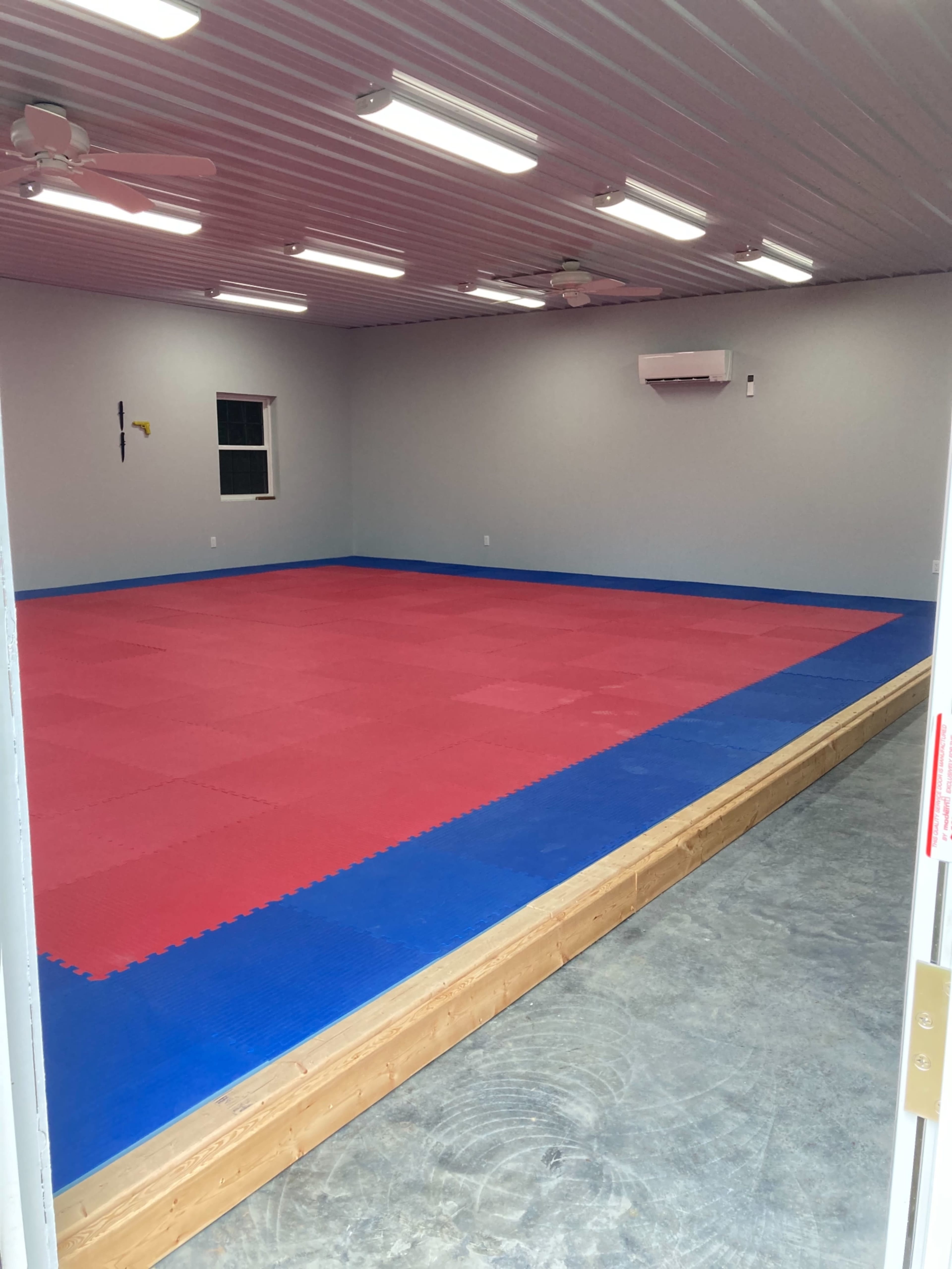 A large, empty room with a red and blue mat floor and a wooden platform along the edges.