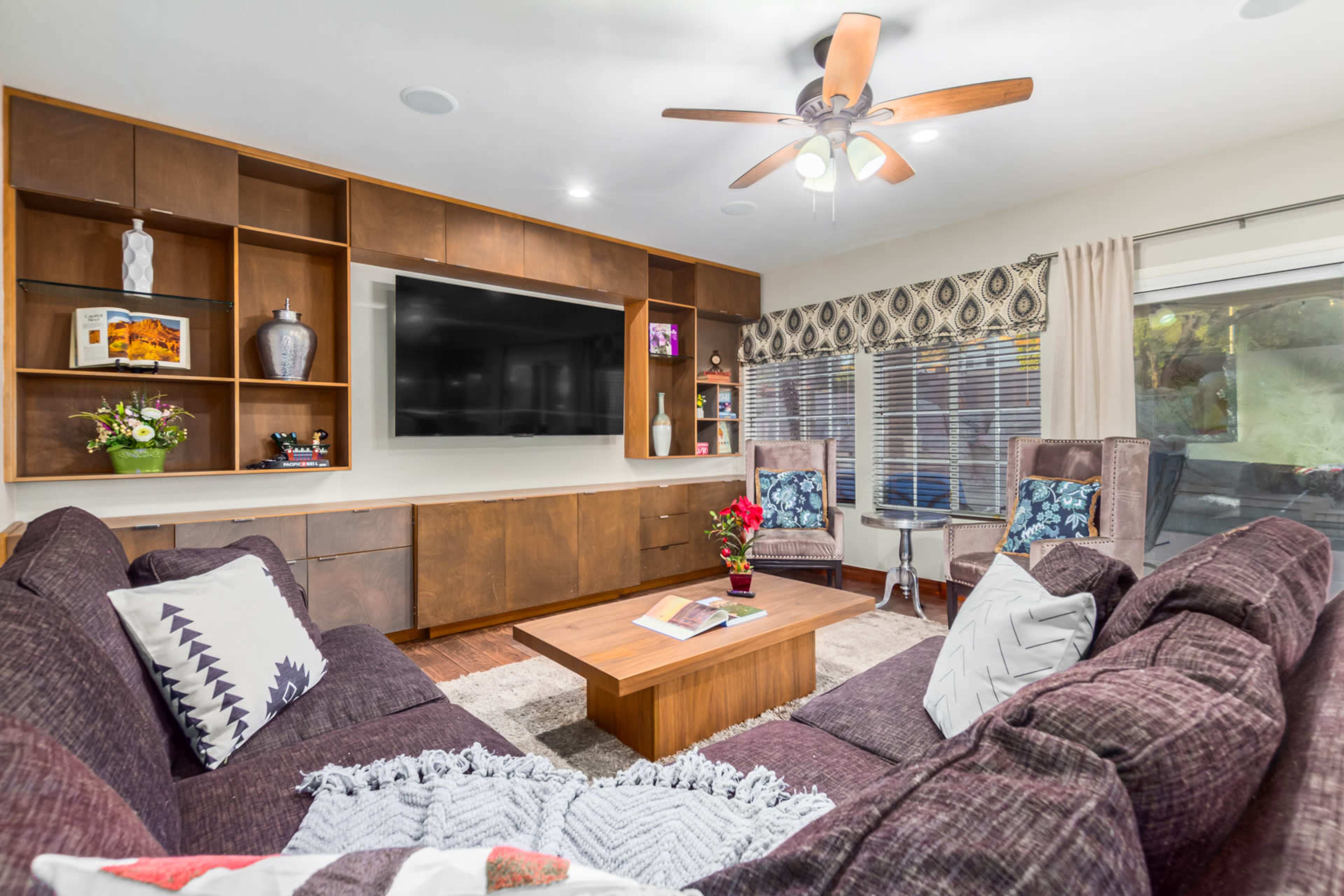 The living room features a large sectional sofa, a wooden entertainment unit with a flat-screen TV, and two armchairs, all arranged around a coffee table.