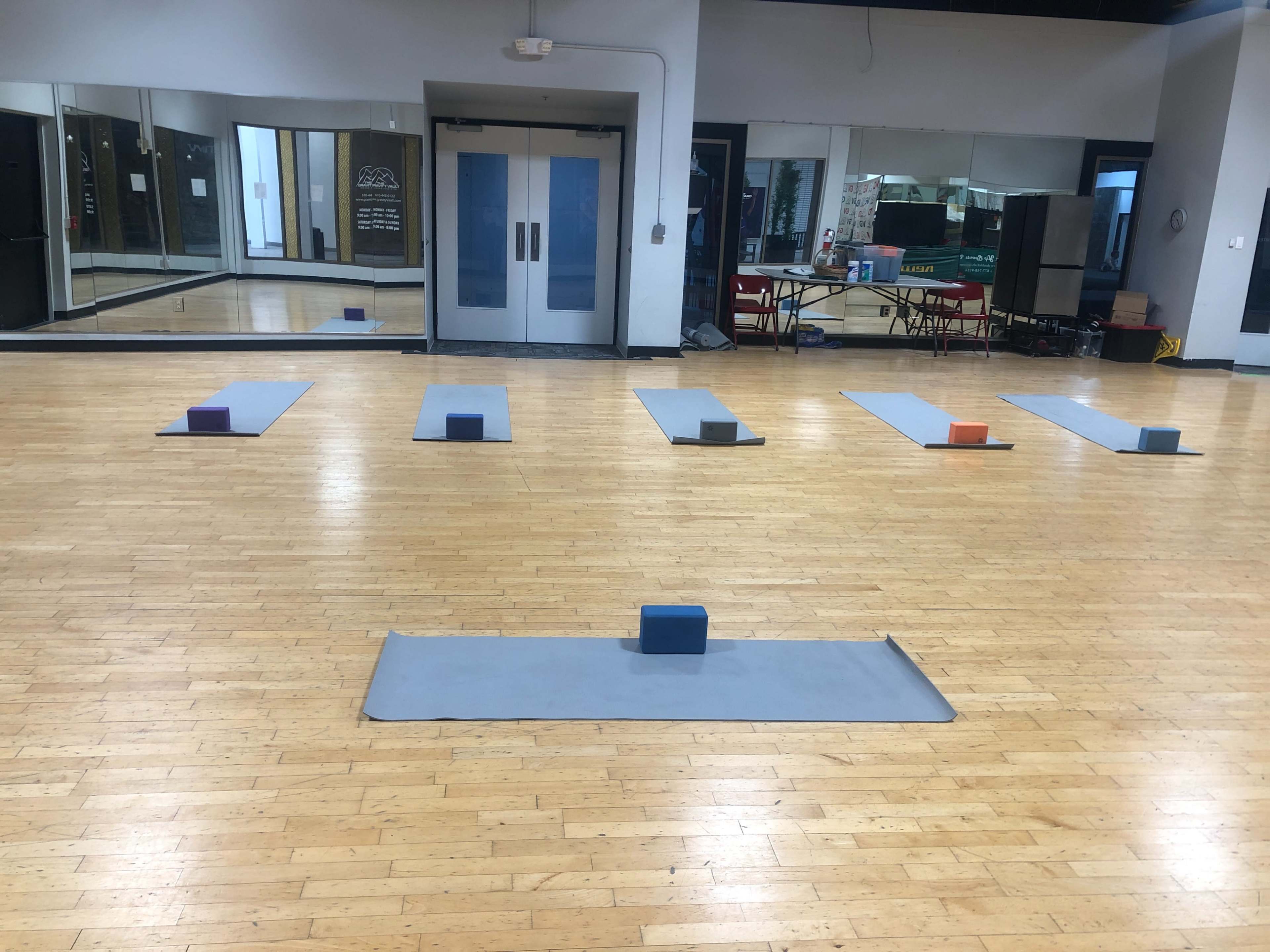 The image shows a spacious yoga studio with several exercise mats, yoga blocks placed on the mats, and large mirrors on the walls.