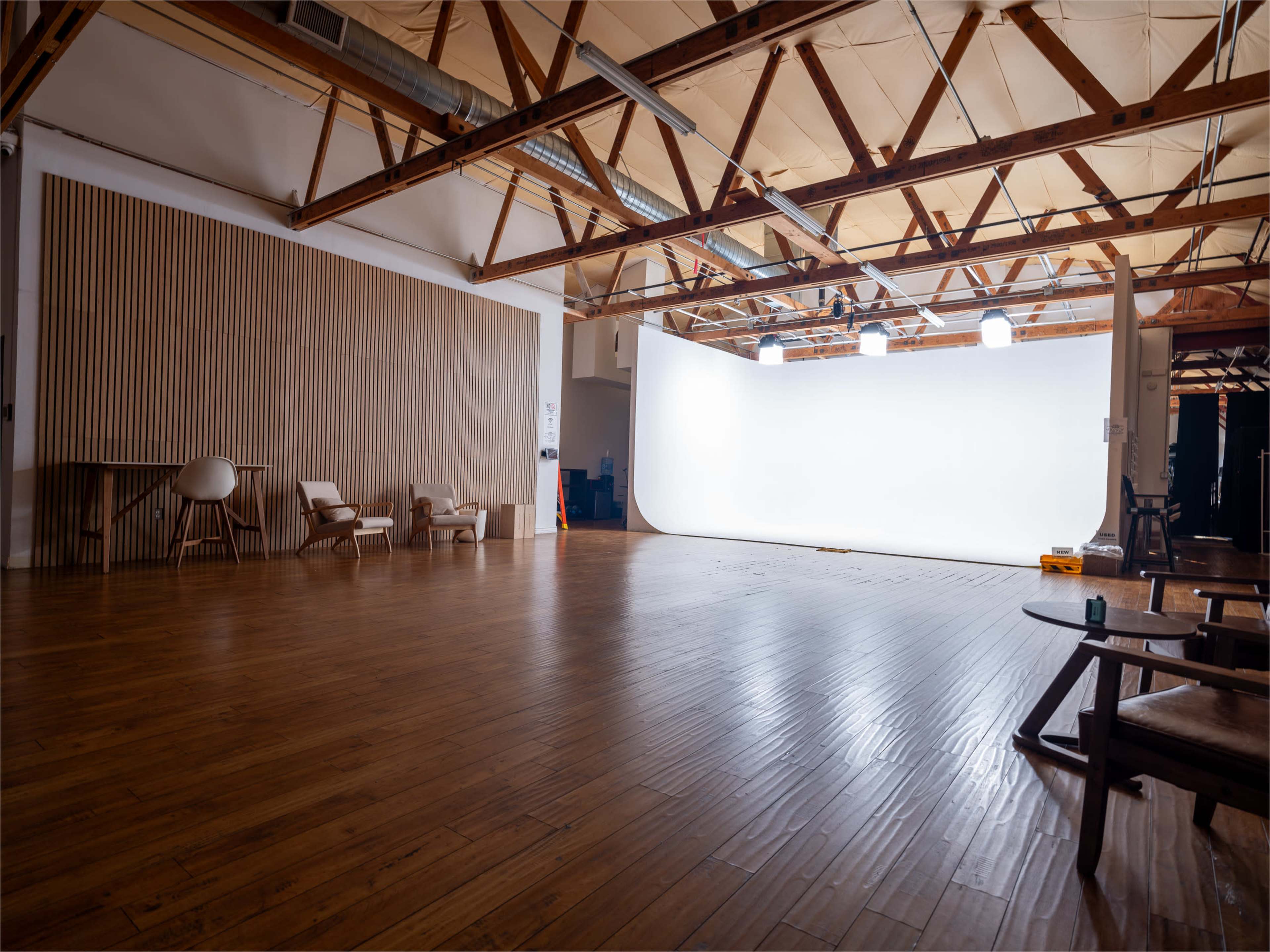 A spacious studio with wooden floors, exposed beams, and a white backdrop setup for photography or filming.
