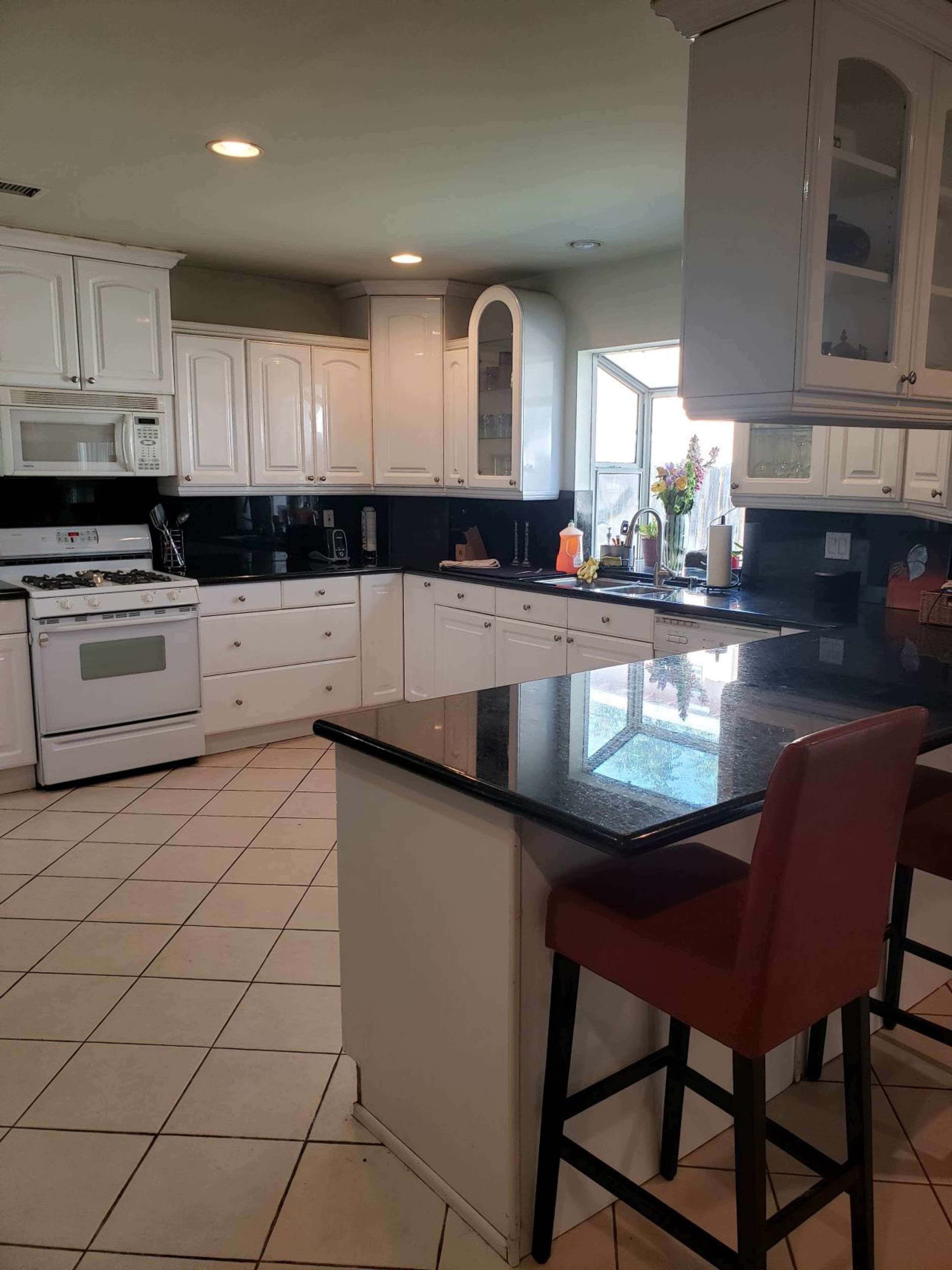 The kitchen features white cabinetry, a black countertop, a window, and a bar stool near the island.