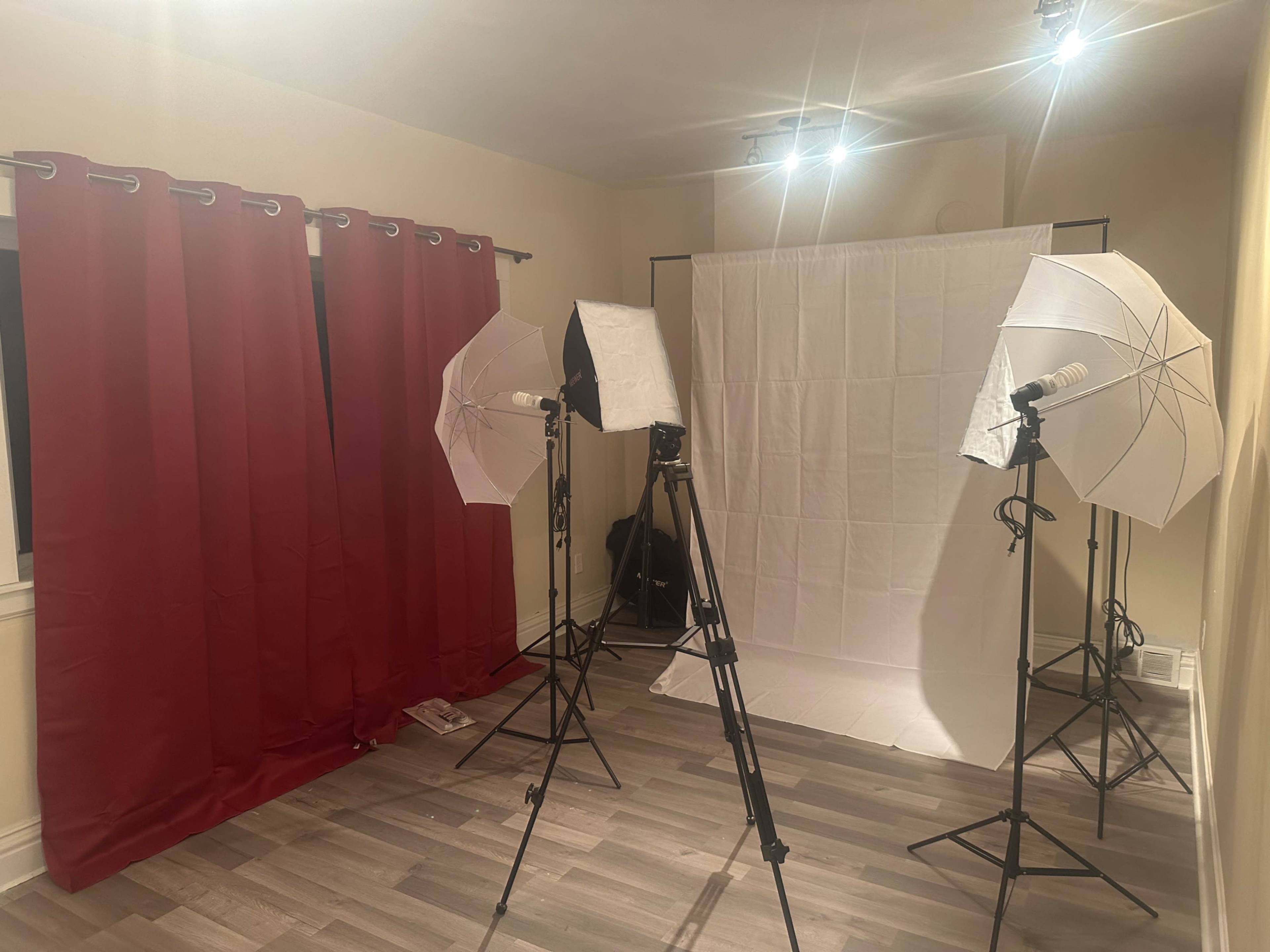The image shows a photography setup in a room with red curtains, including two light umbrellas, tripods, and a white backdrop.