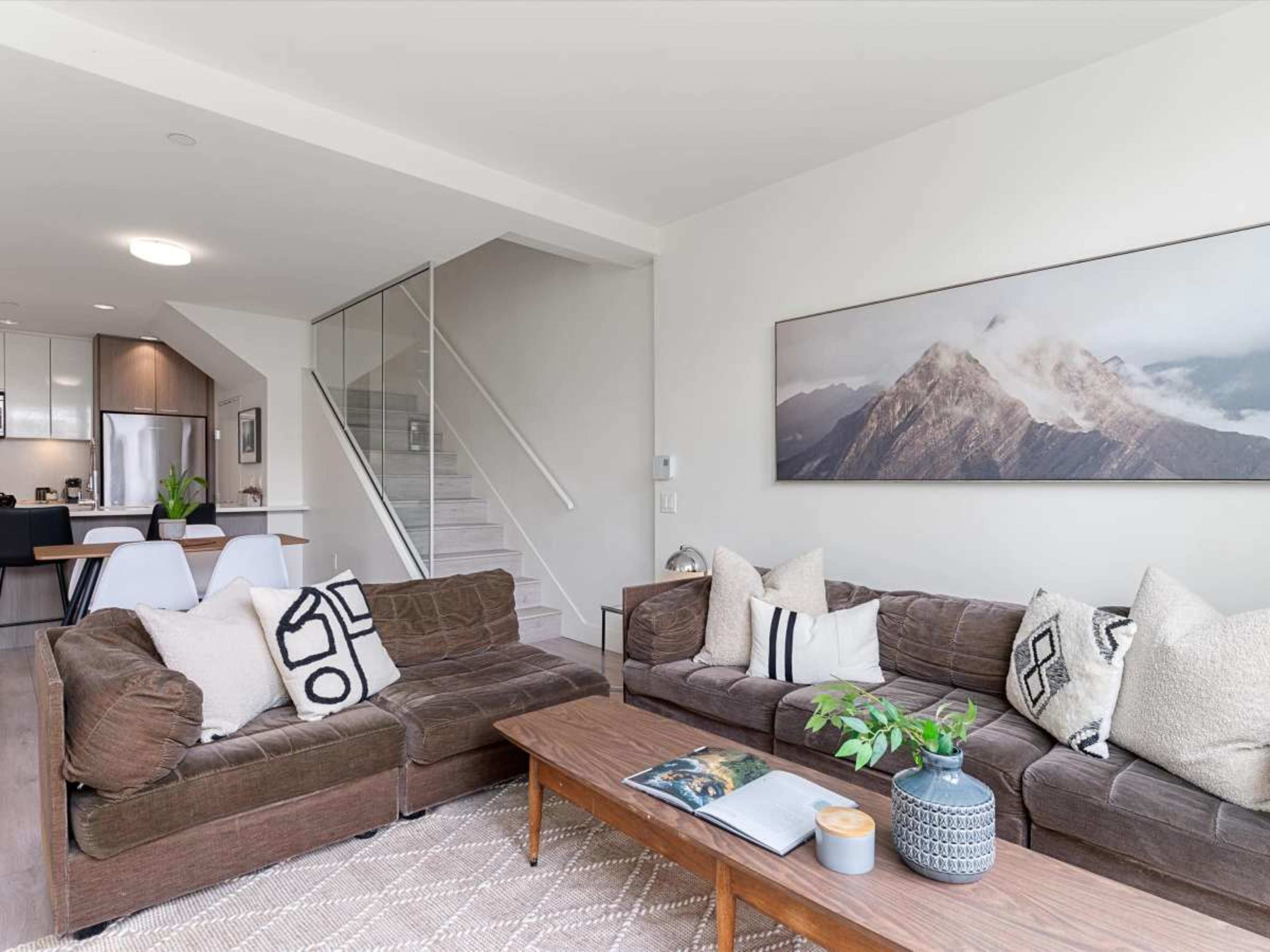 The living room features two brown sofas with patterned pillows, a wooden coffee table, and a mountain landscape artwork on the wall.