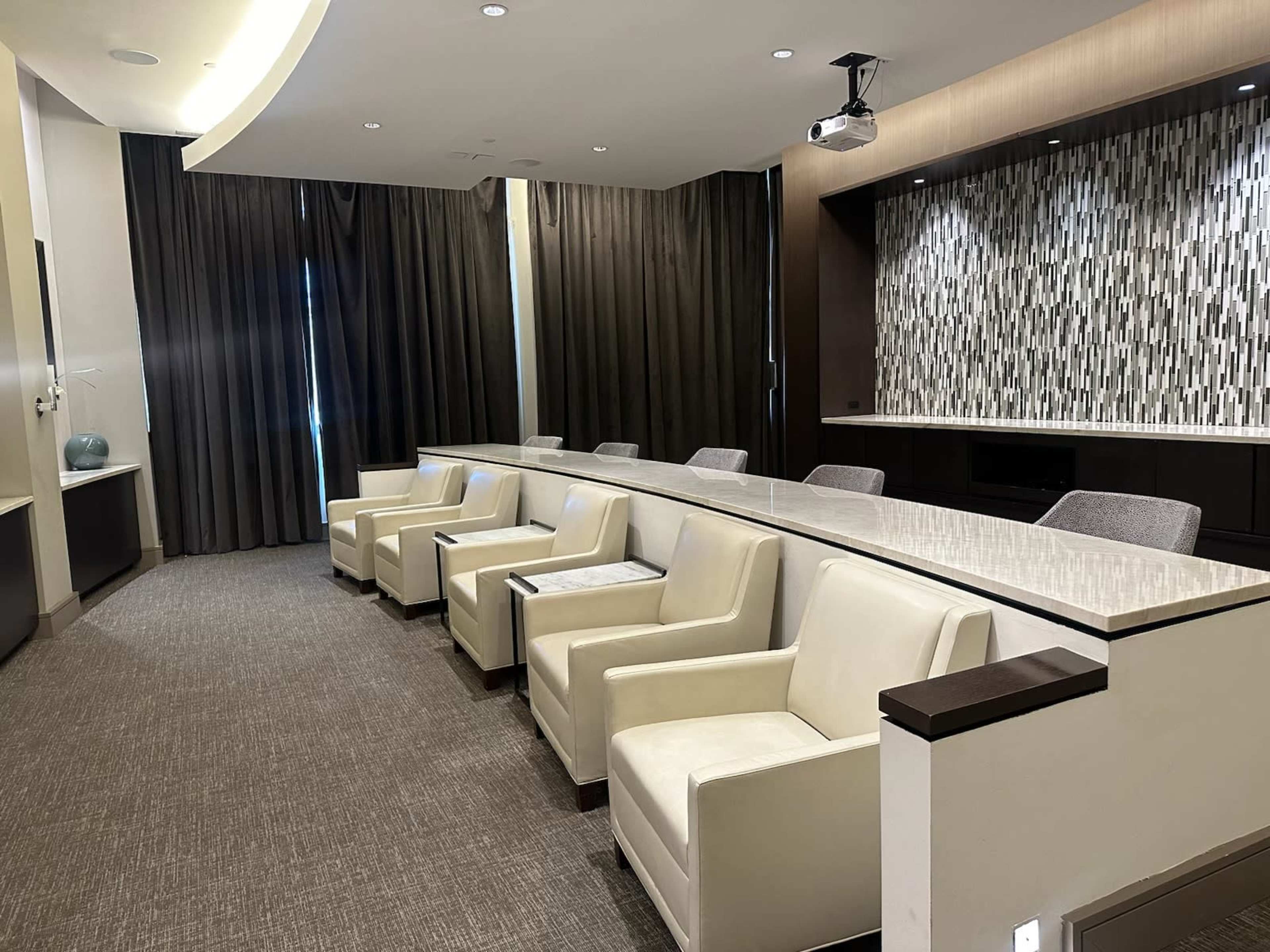 A modern conference room with a long white table, several cream-colored chairs, and dark curtains on the windows.