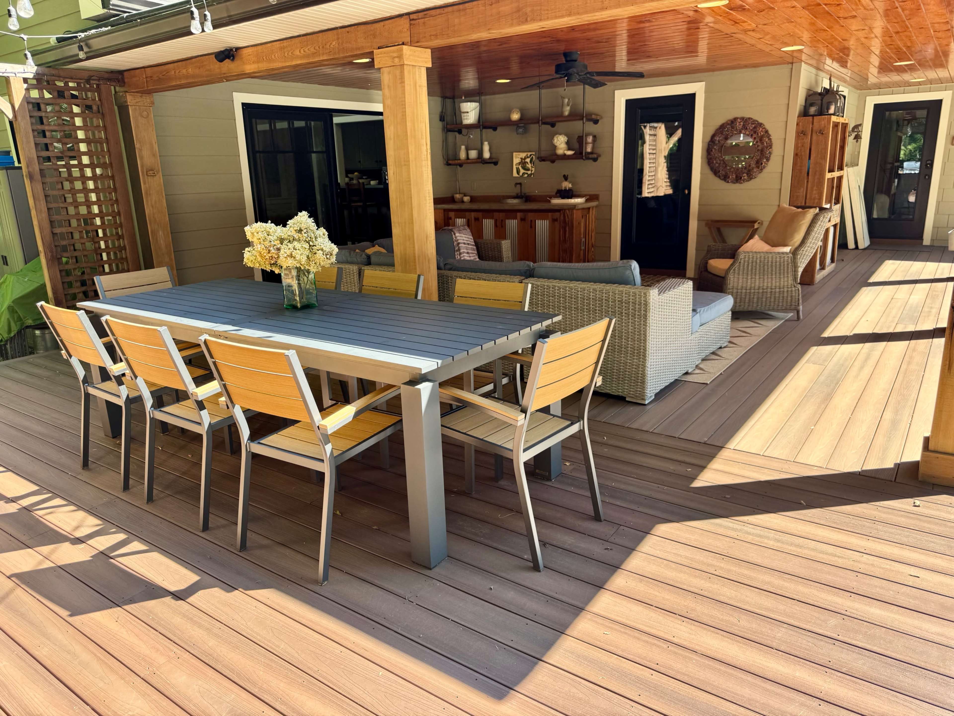 A spacious outdoor patio features a large dining table with yellow chairs, surrounded by comfortable seating and a bar area.