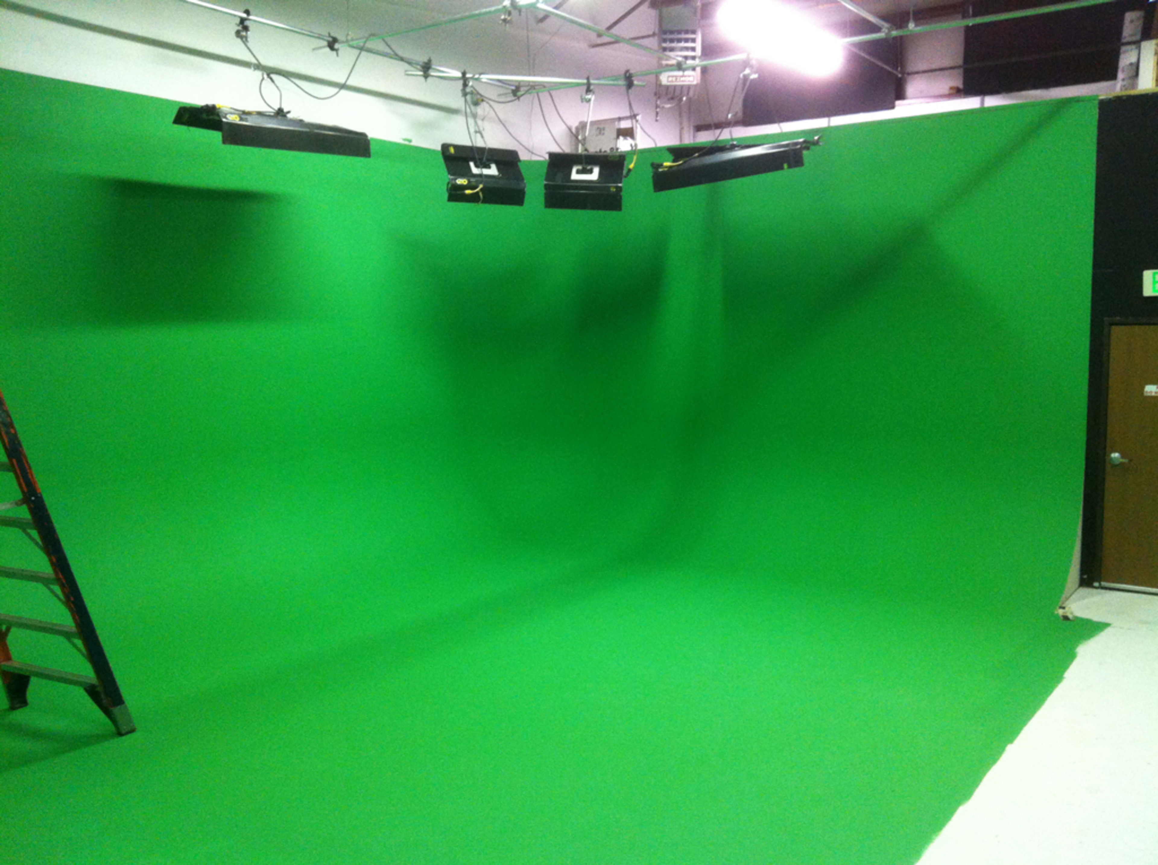 A green screen studio with a large green backdrop and lighting fixtures overhead.