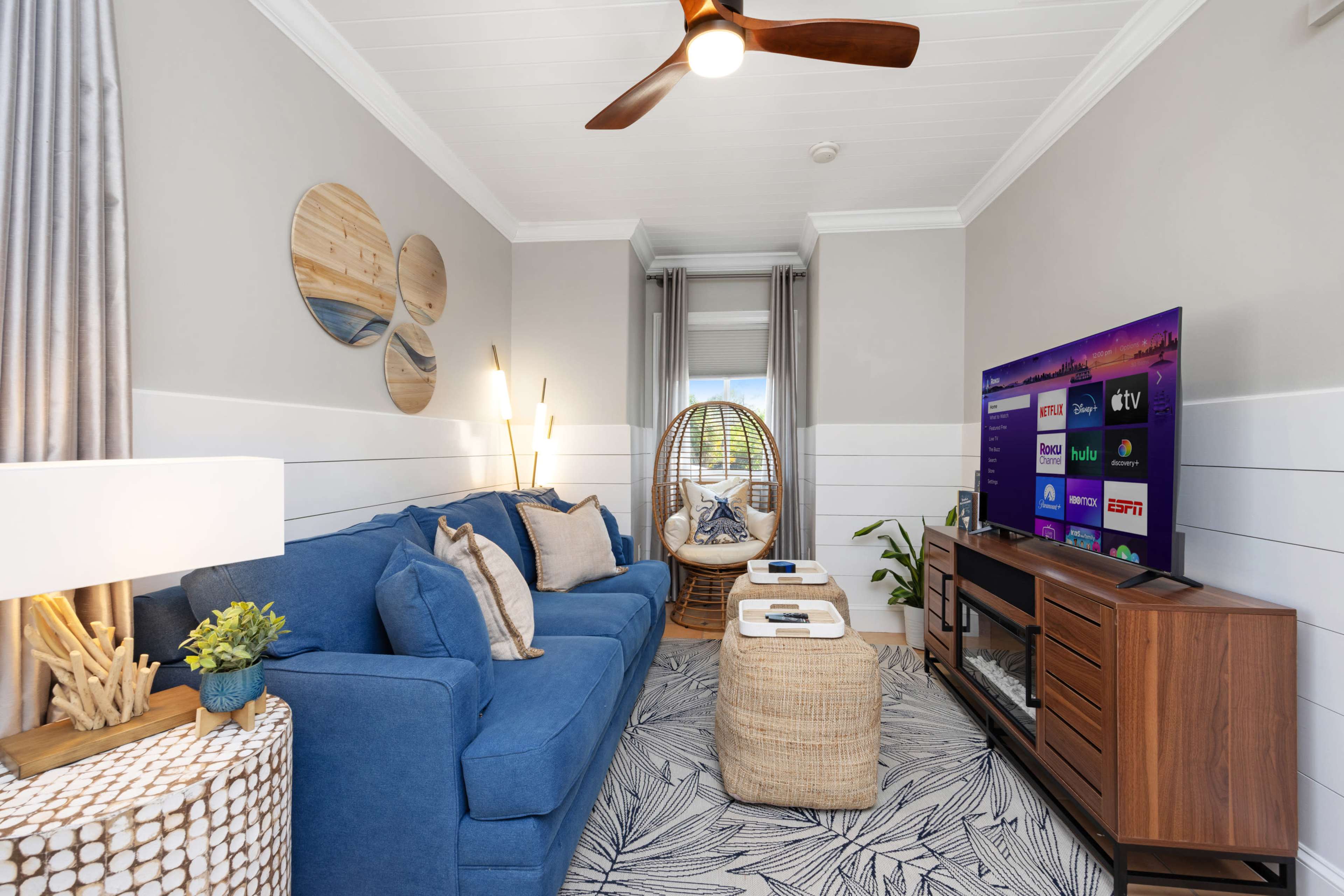 A cozy living room features a blue sofa, a wooden coffee table, a large television, and a comfortable hanging chair near a window.
