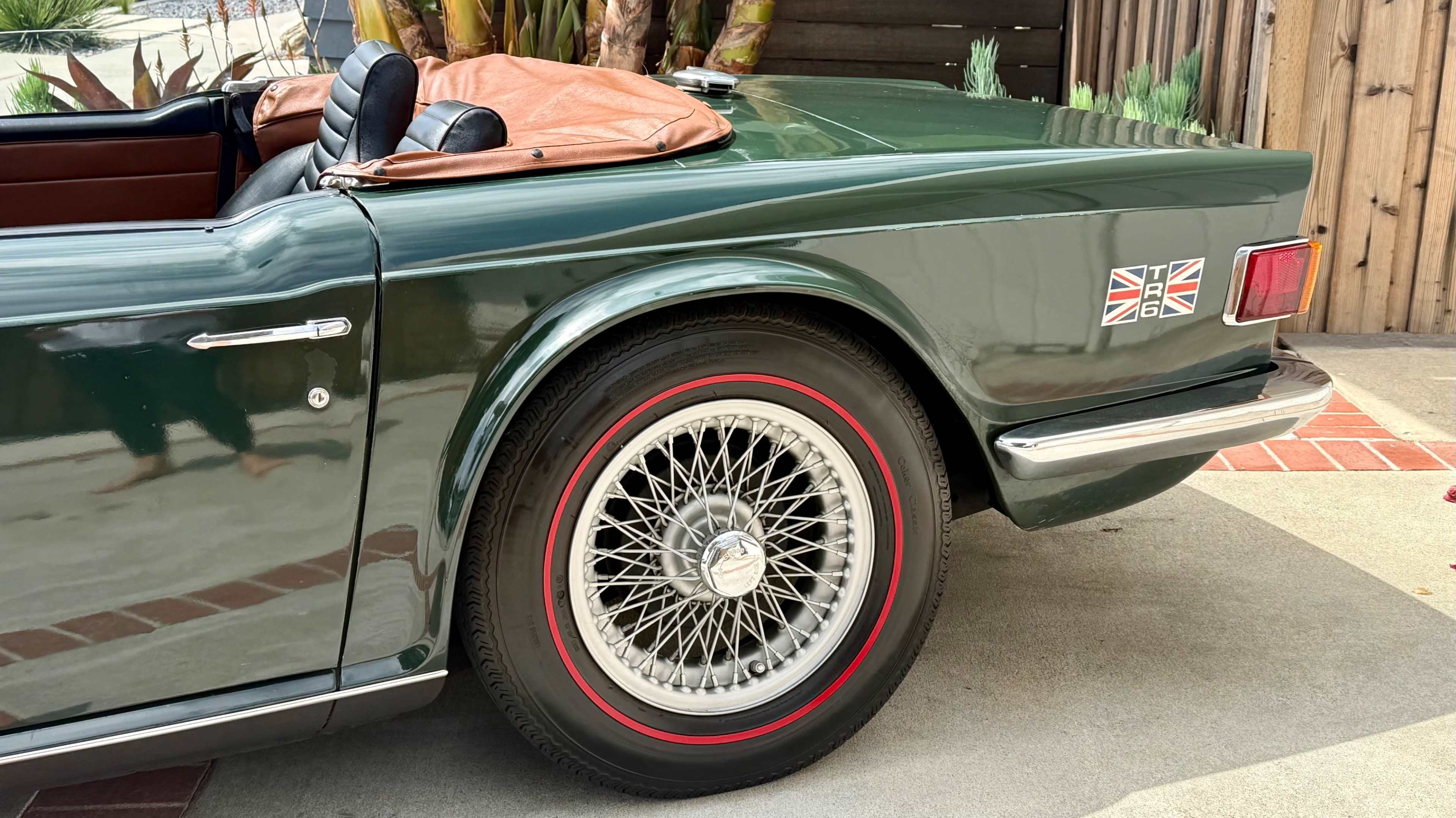 The image shows the rear side of a vintage green convertible car with a wire-spoke wheel and a British flag emblem on the trunk.