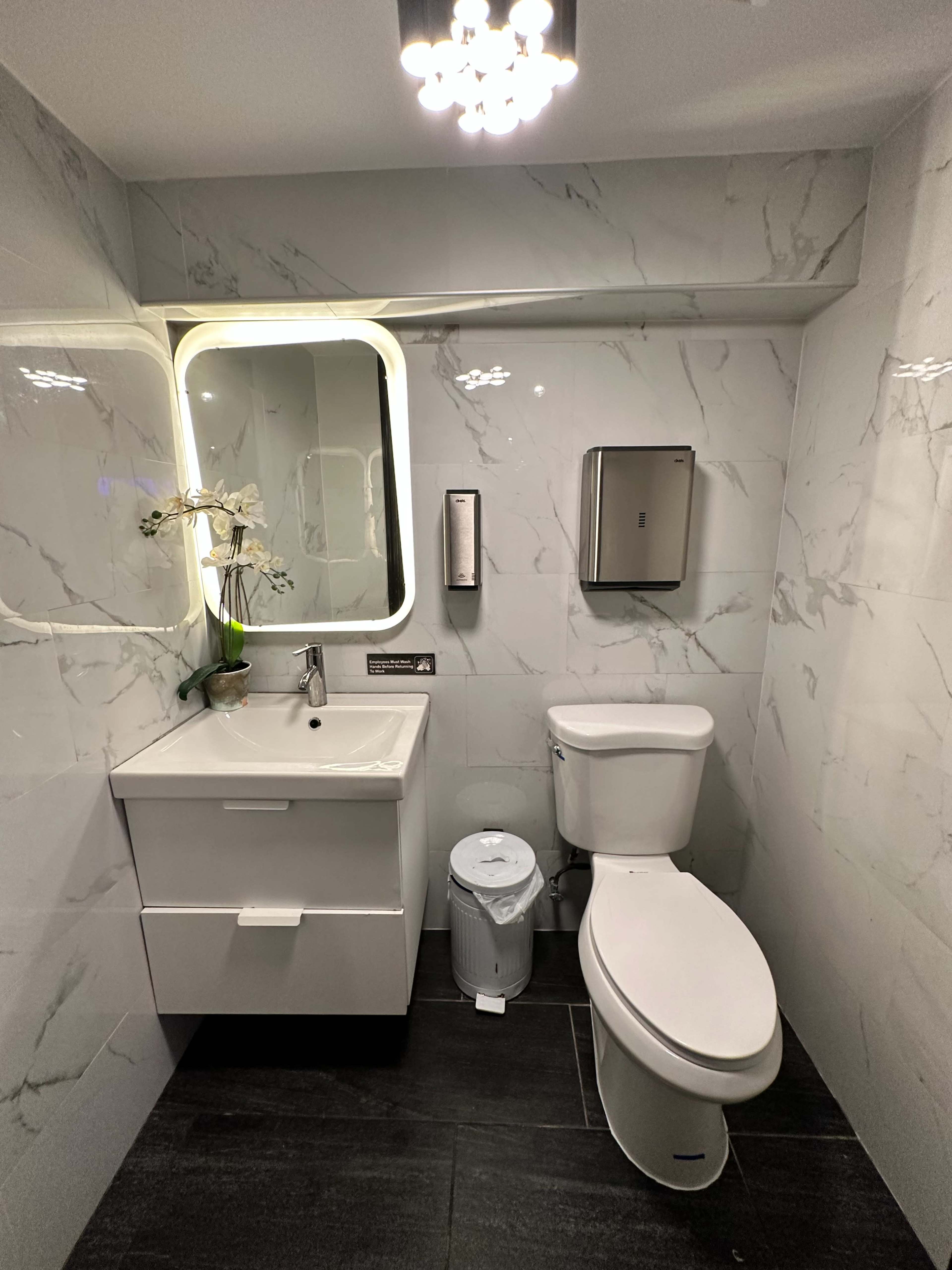 A modern bathroom featuring a toilet, a sink with a cabinet, a mirror, and marble-patterned walls.