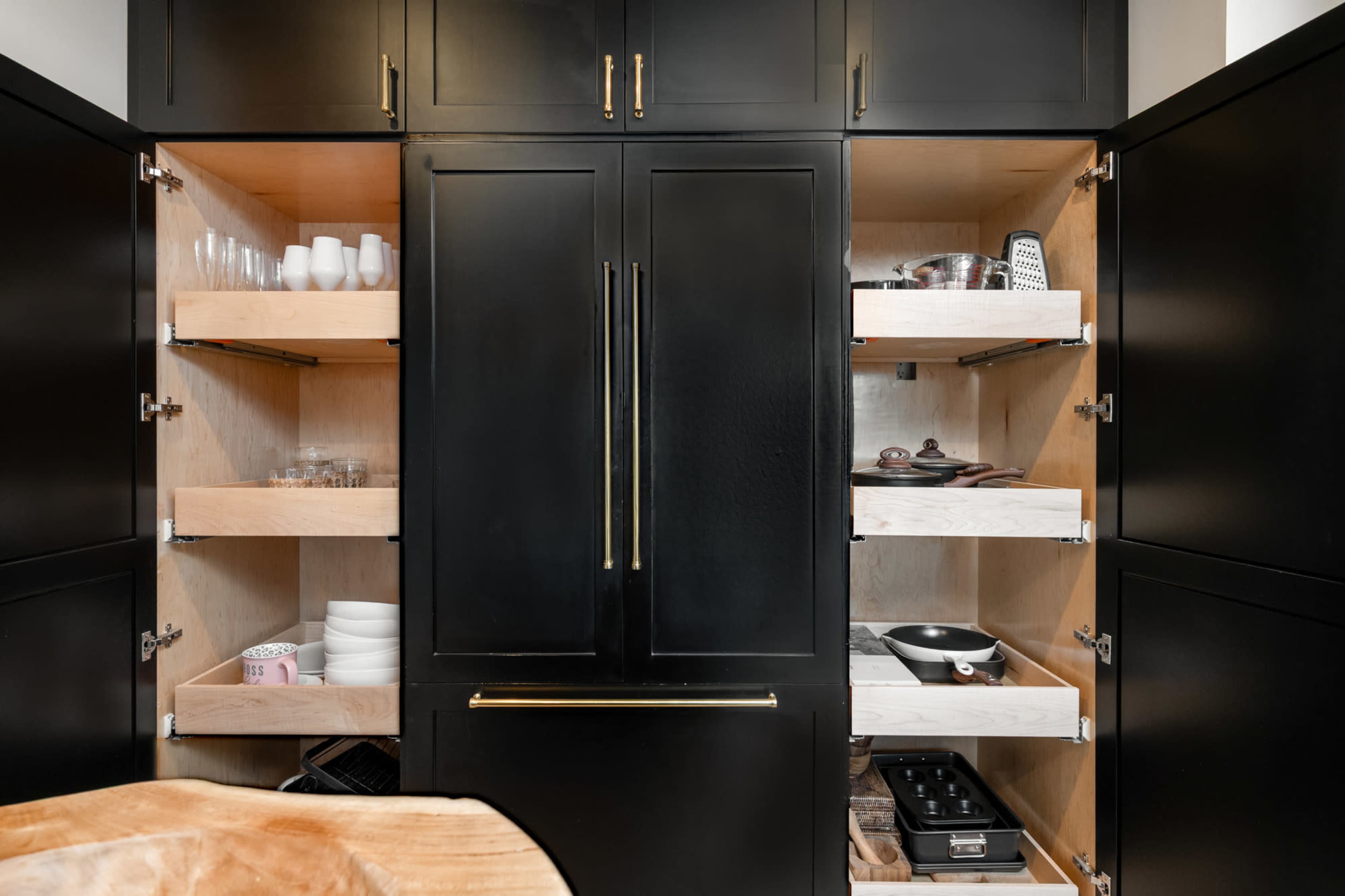 The image shows a black kitchen pantry with wooden shelves containing various dishes, glassware, and cooking utensils.