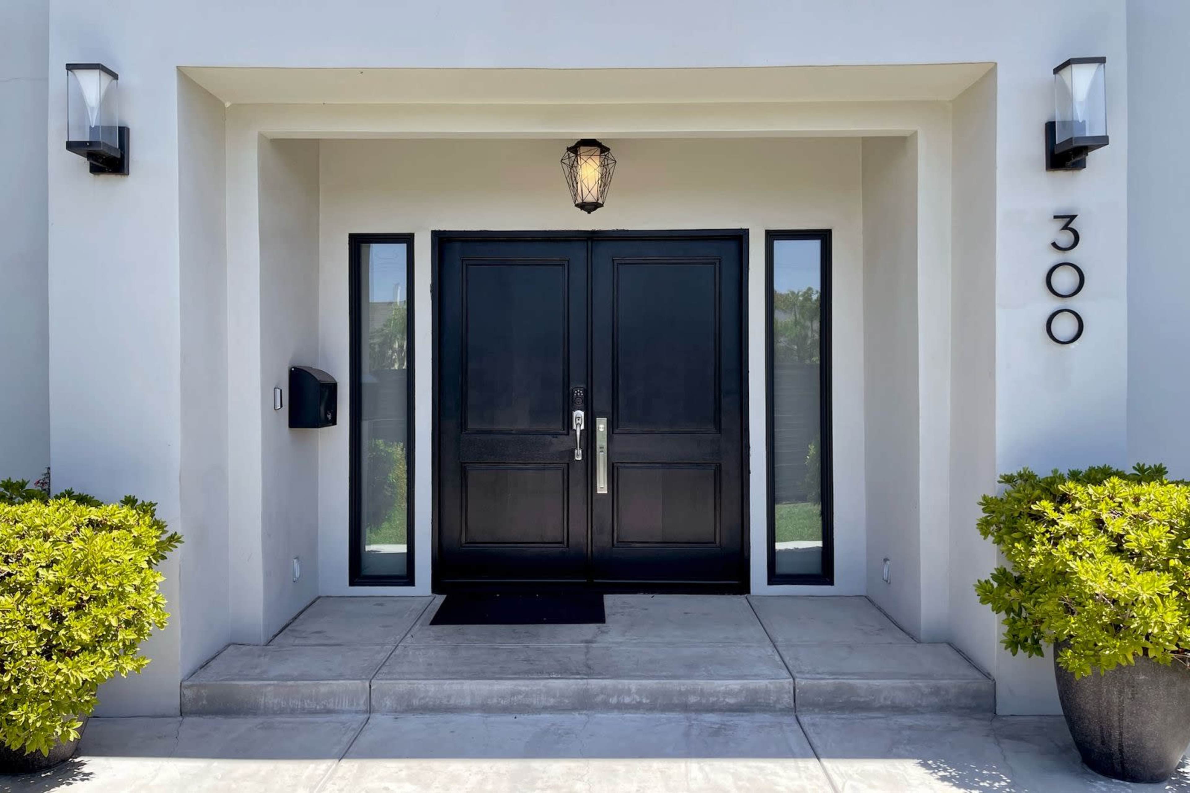 The entrance features a pair of black double doors, flanked by two large windows, with a light fixture above and small shrubs on either side.