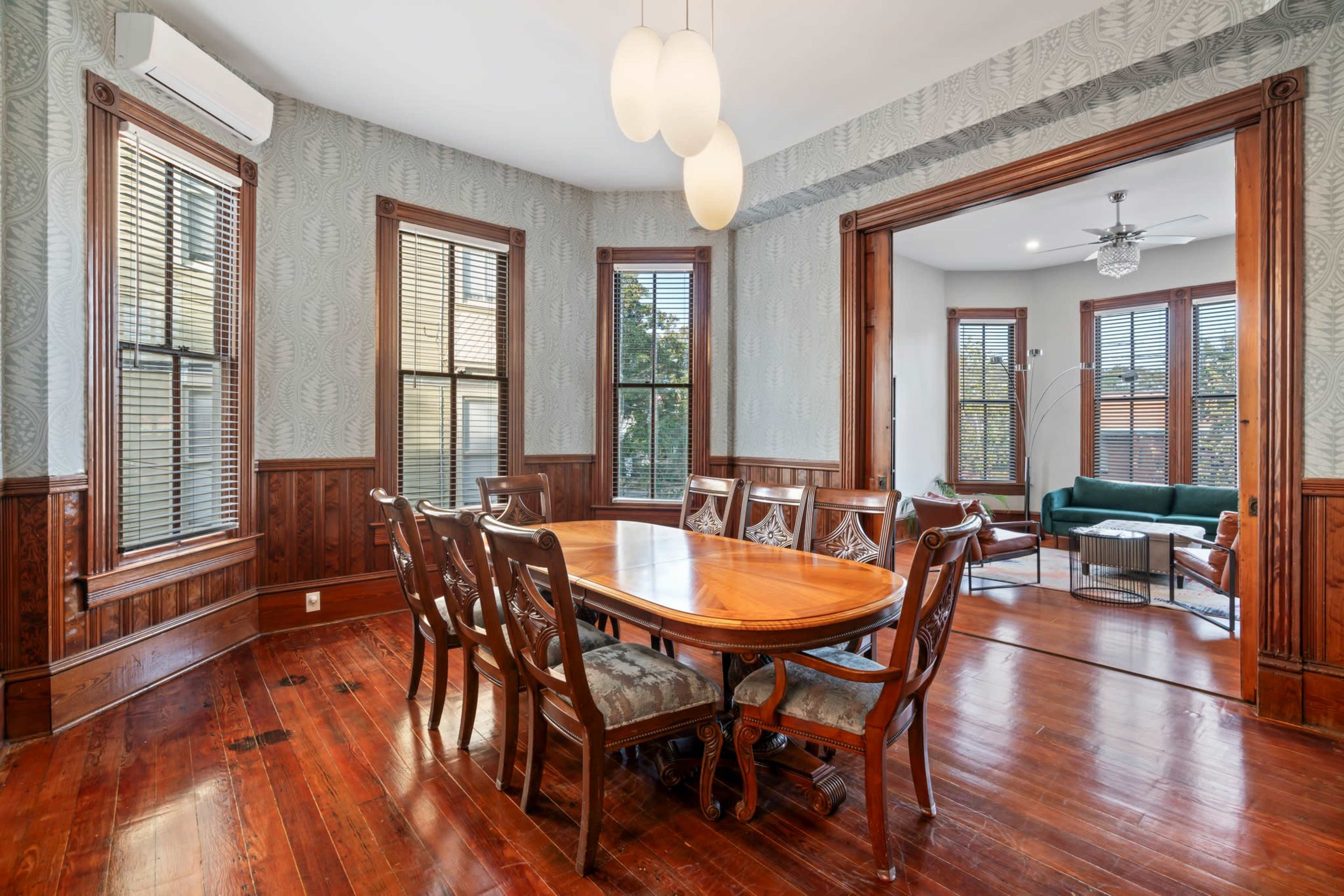 A spacious dining room features a wooden table surrounded by chairs, with large windows allowing natural light to fill the space.