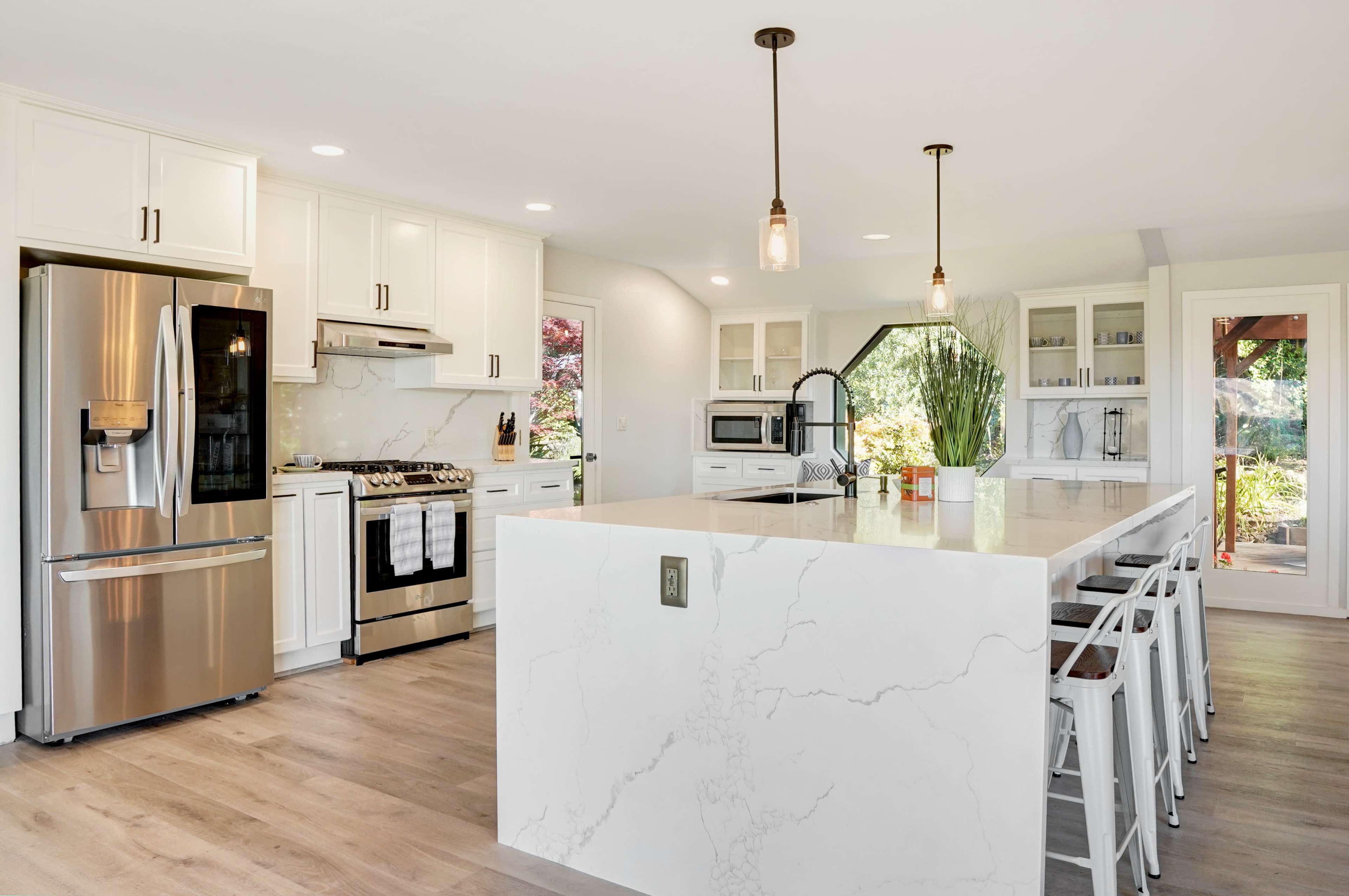 A modern kitchen features white cabinetry, stainless steel appliances, and a large island with marble-like countertops.