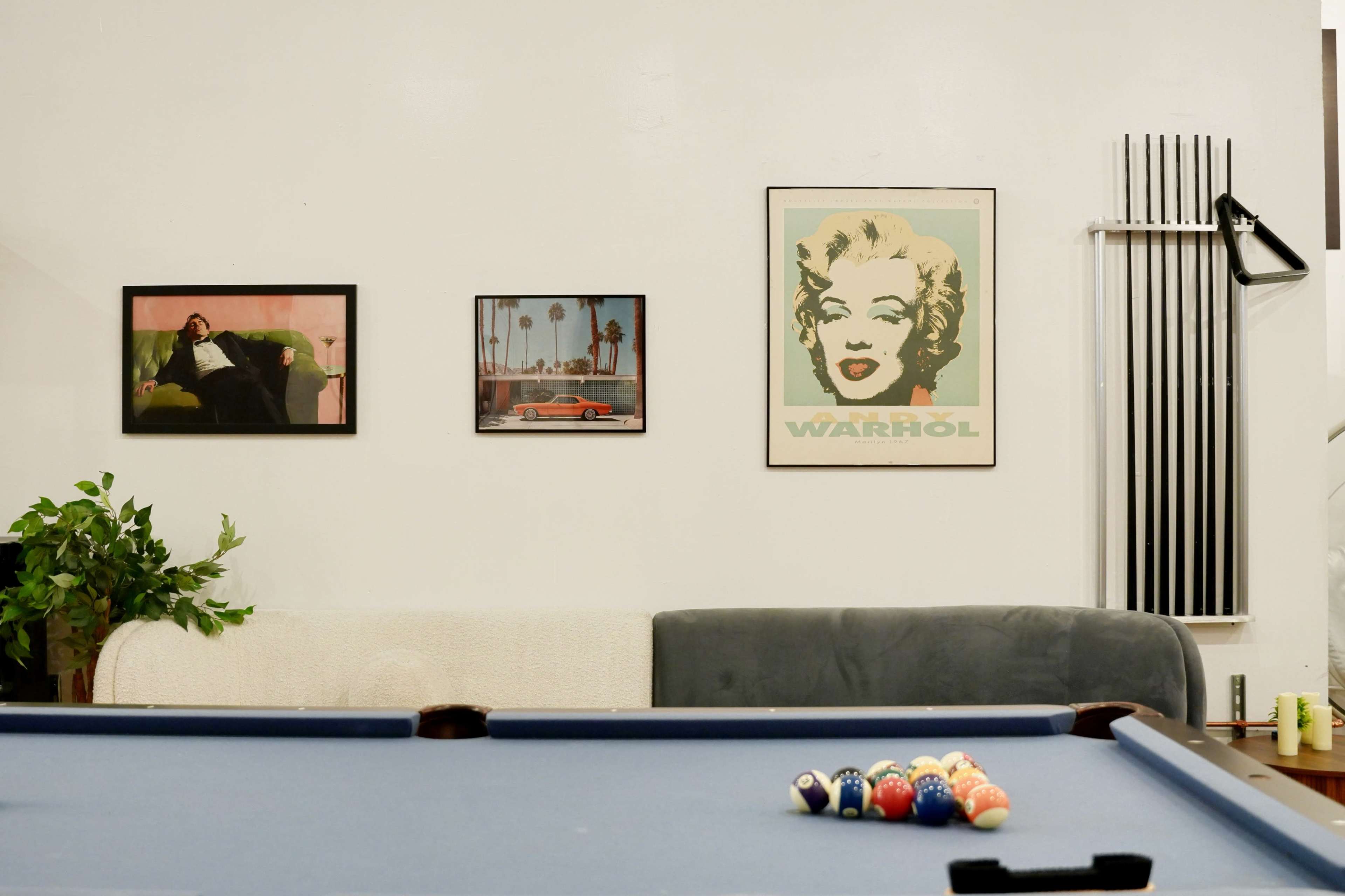 The image features a pool table in the foreground with colorful billiard balls arranged on it, while three framed pictures hang on the wall behind a sofa.