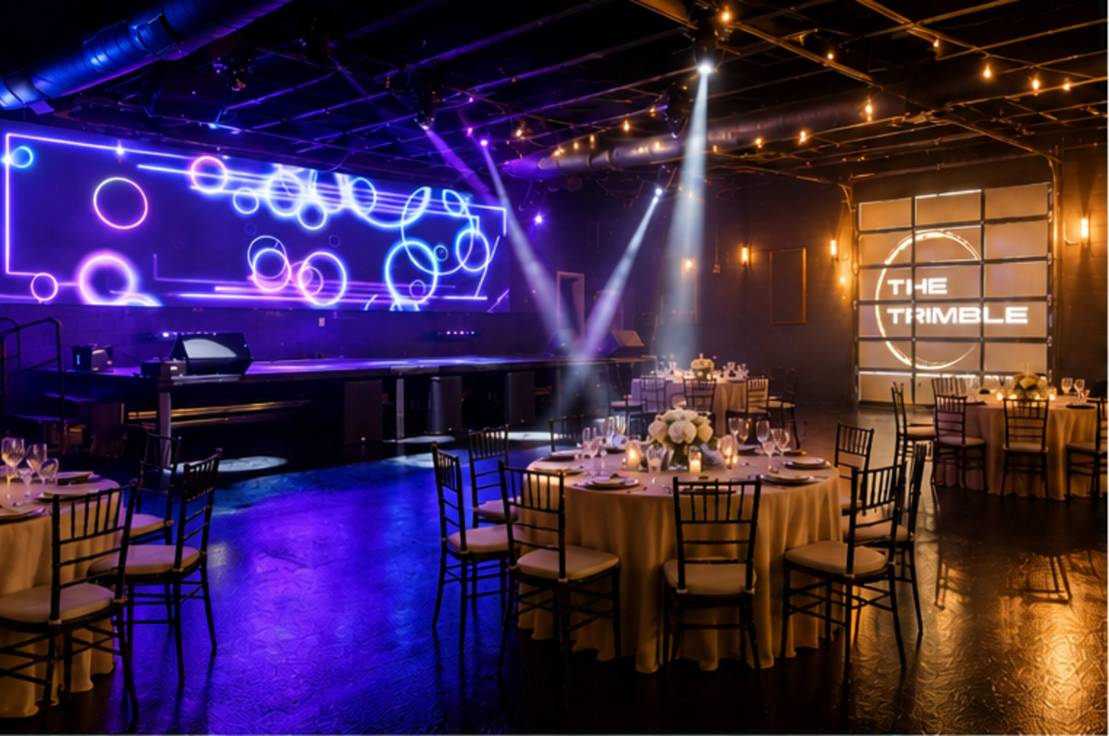 A modern event space features elegantly set round tables and a vibrant light display on the wall, creating an atmosphere for gatherings.