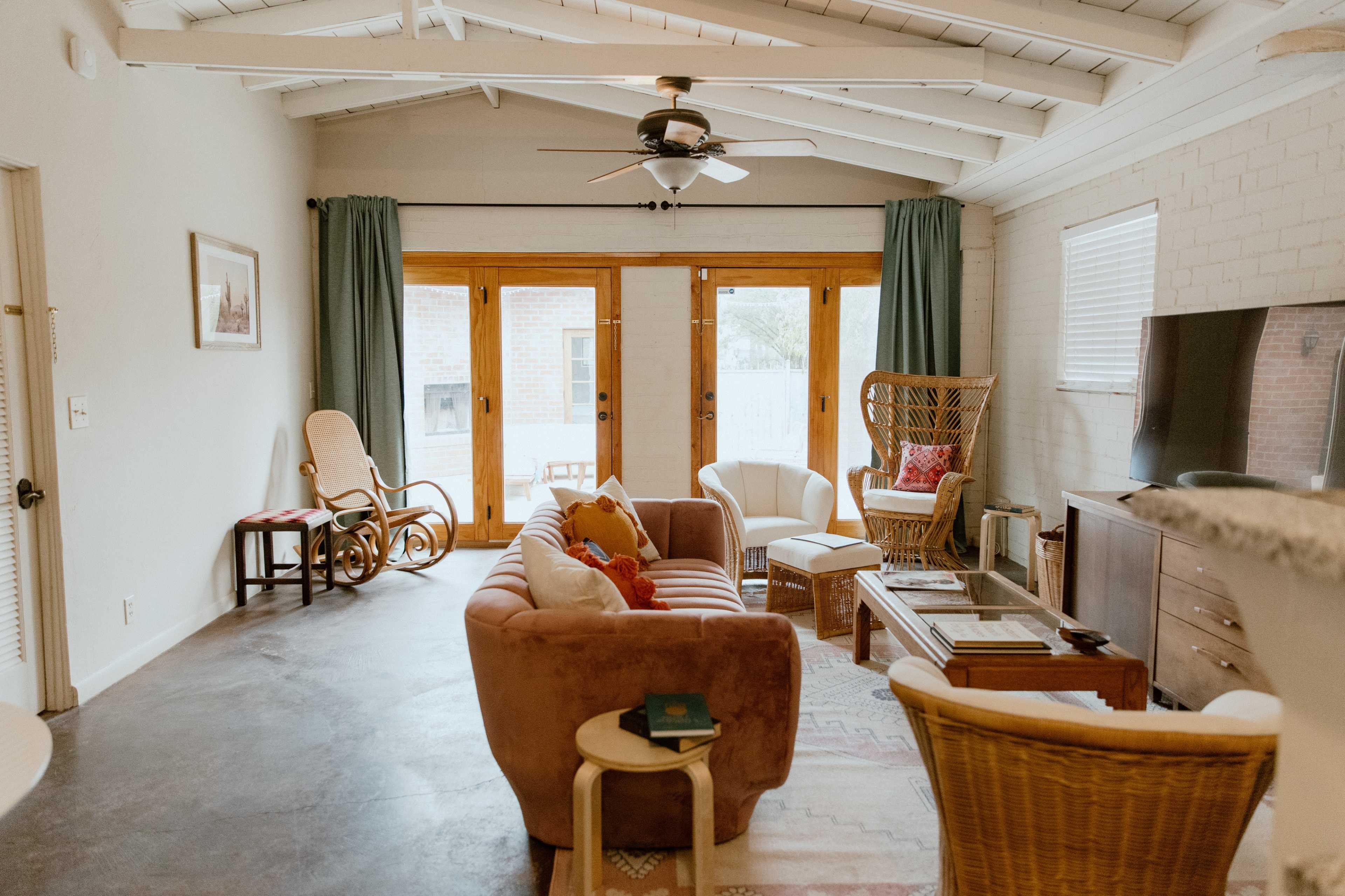 The image shows a living room with a brown sectional sofa, light-colored walls, a ceiling fan, and large windows with sliding glass doors.