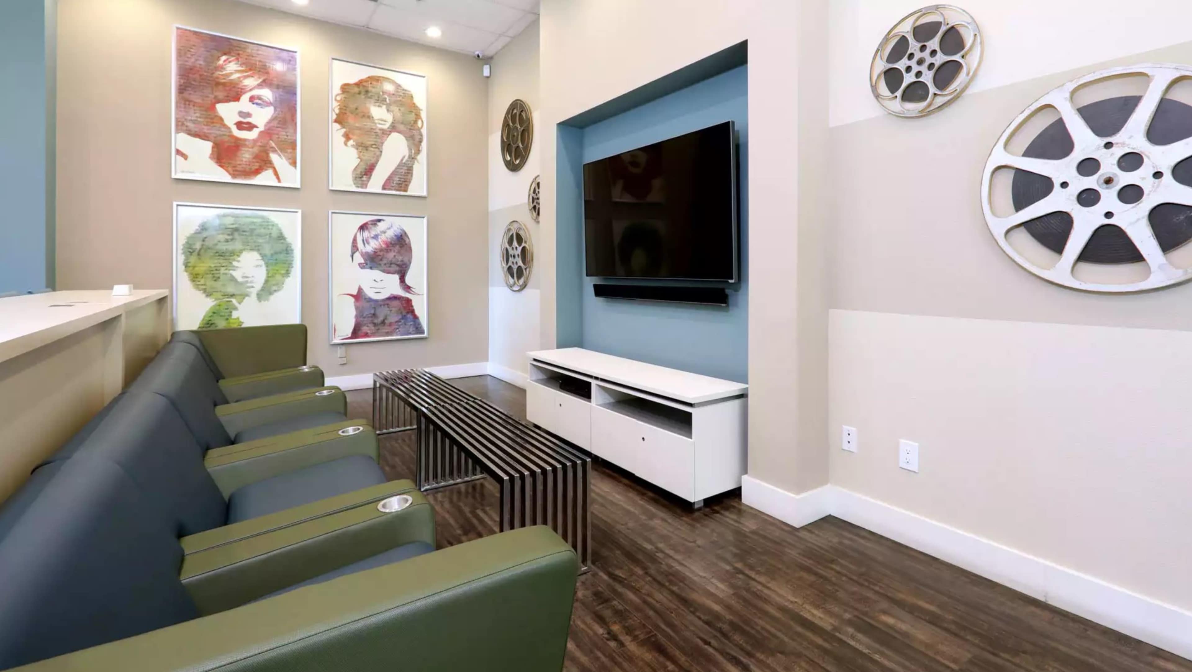A modern waiting area featuring green seating, a television mounted on the wall, and framed art pieces alongside film reels displayed decoratively.