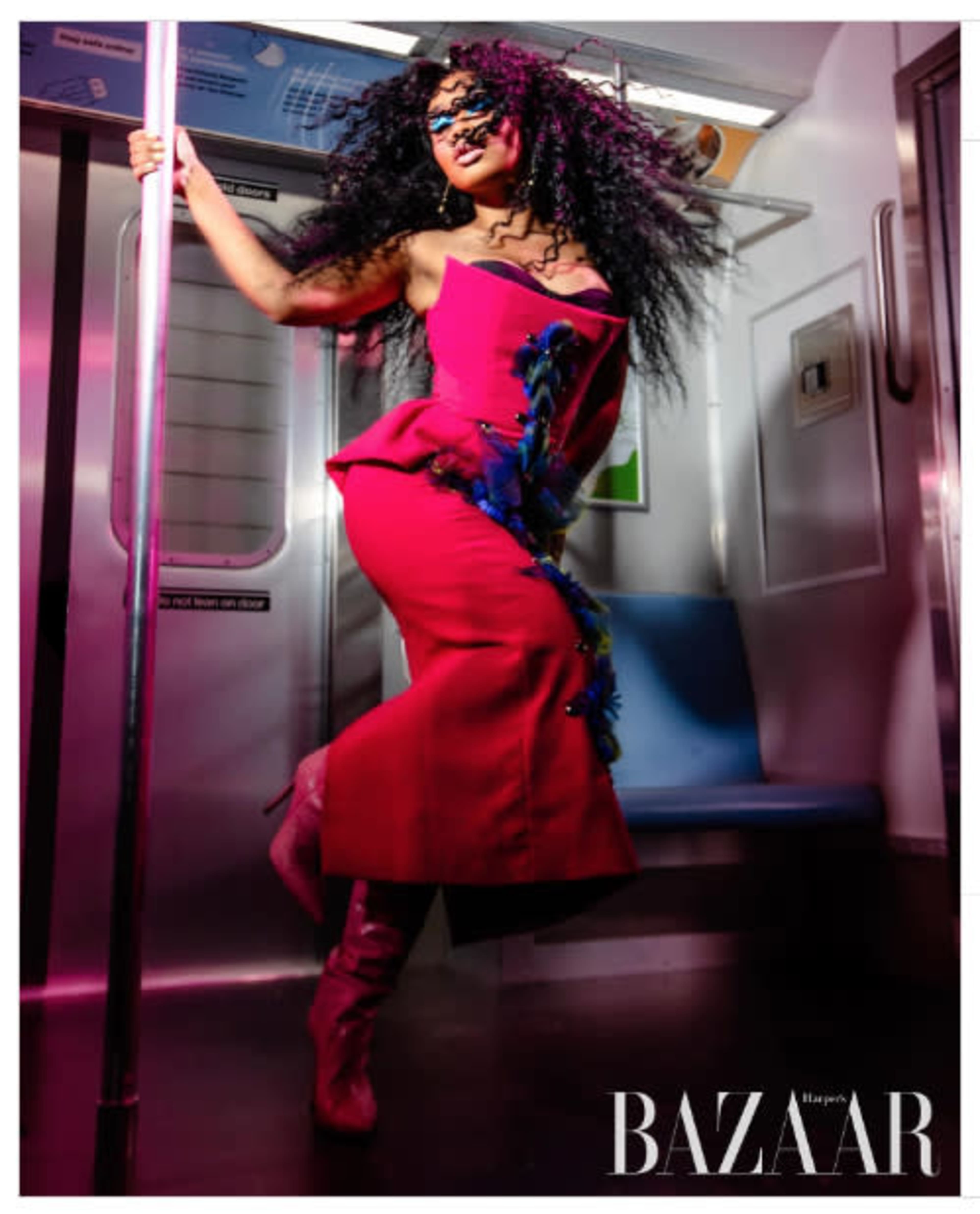 A person in a pink dress and matching knee-high boots poses energetically on a subway train.