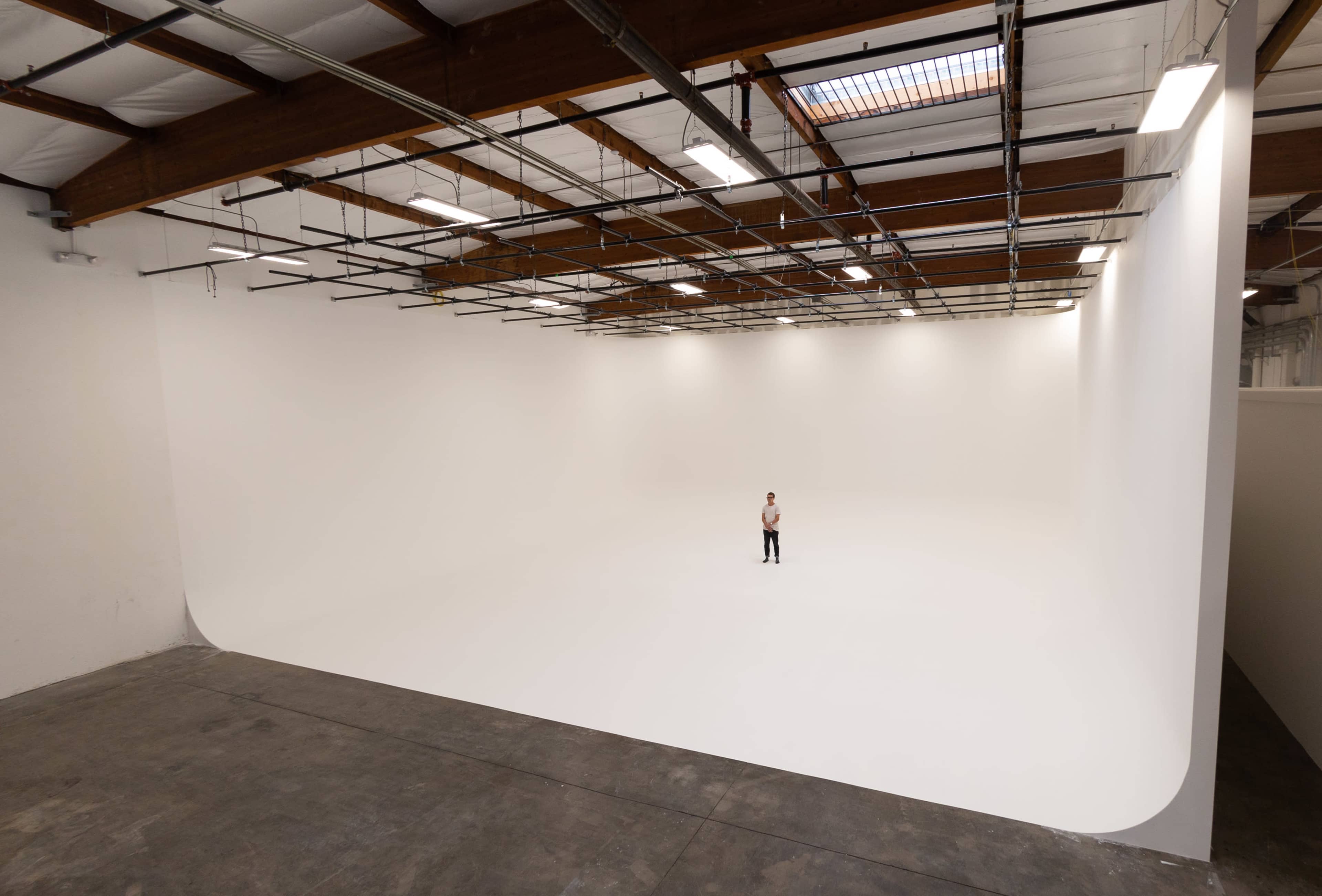 A person stands alone in a large, empty studio with white walls and a curved backdrop.