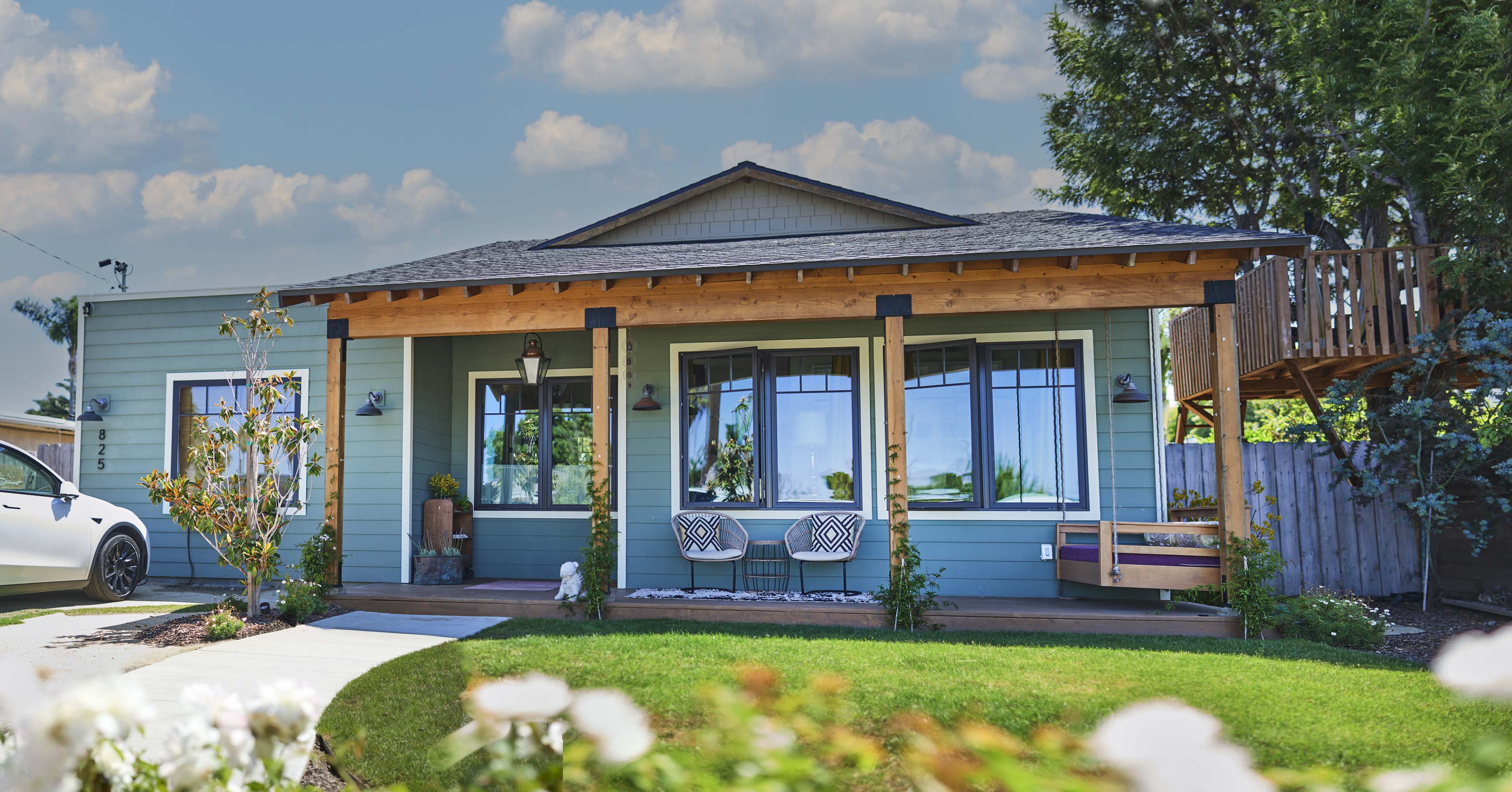 A blue house with a front porch, two decorative chairs, and a garden of white flowers.
