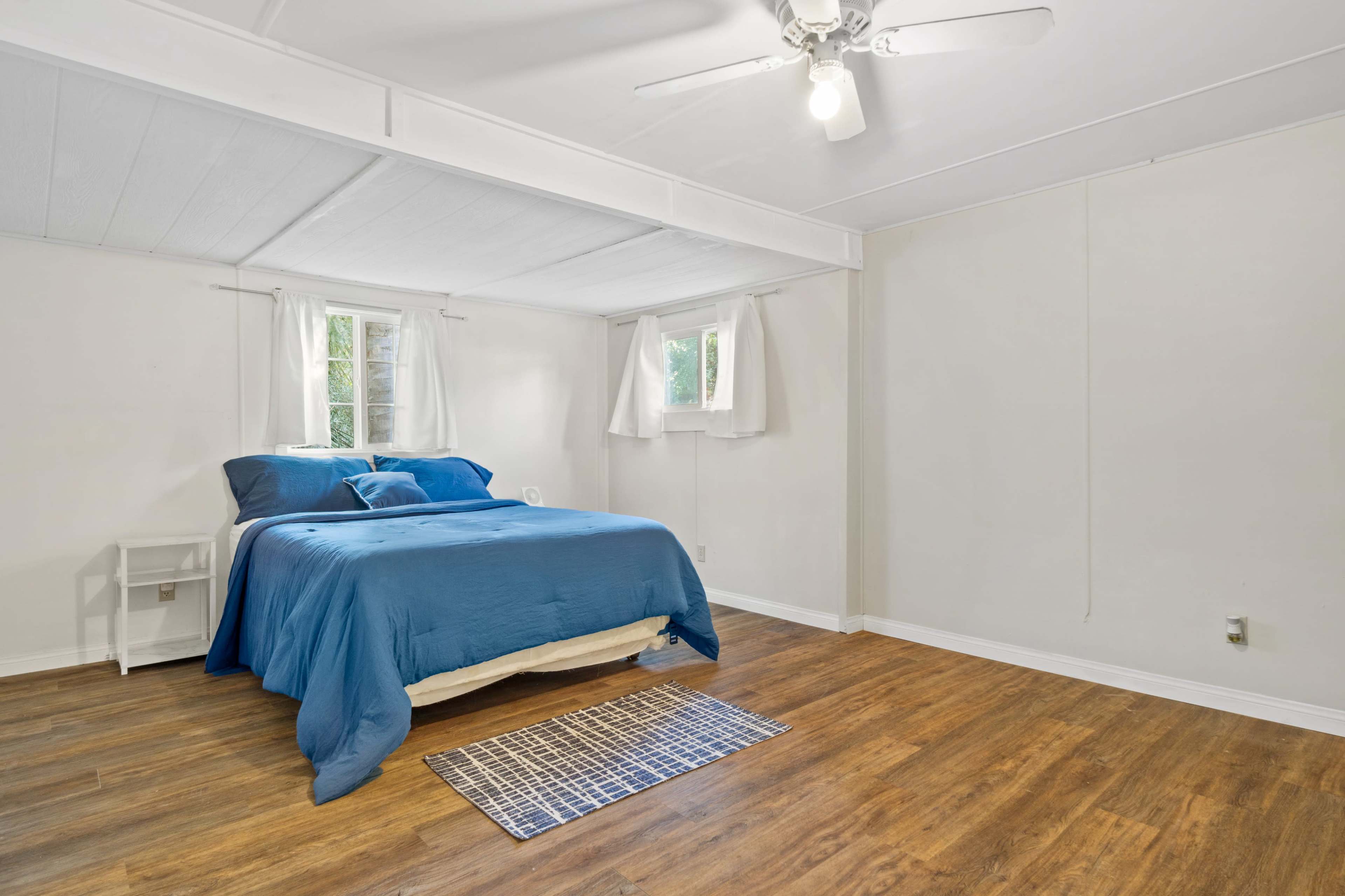 A simple bedroom featuring a bed with a blue comforter, two windows, and a light fixture on the ceiling.